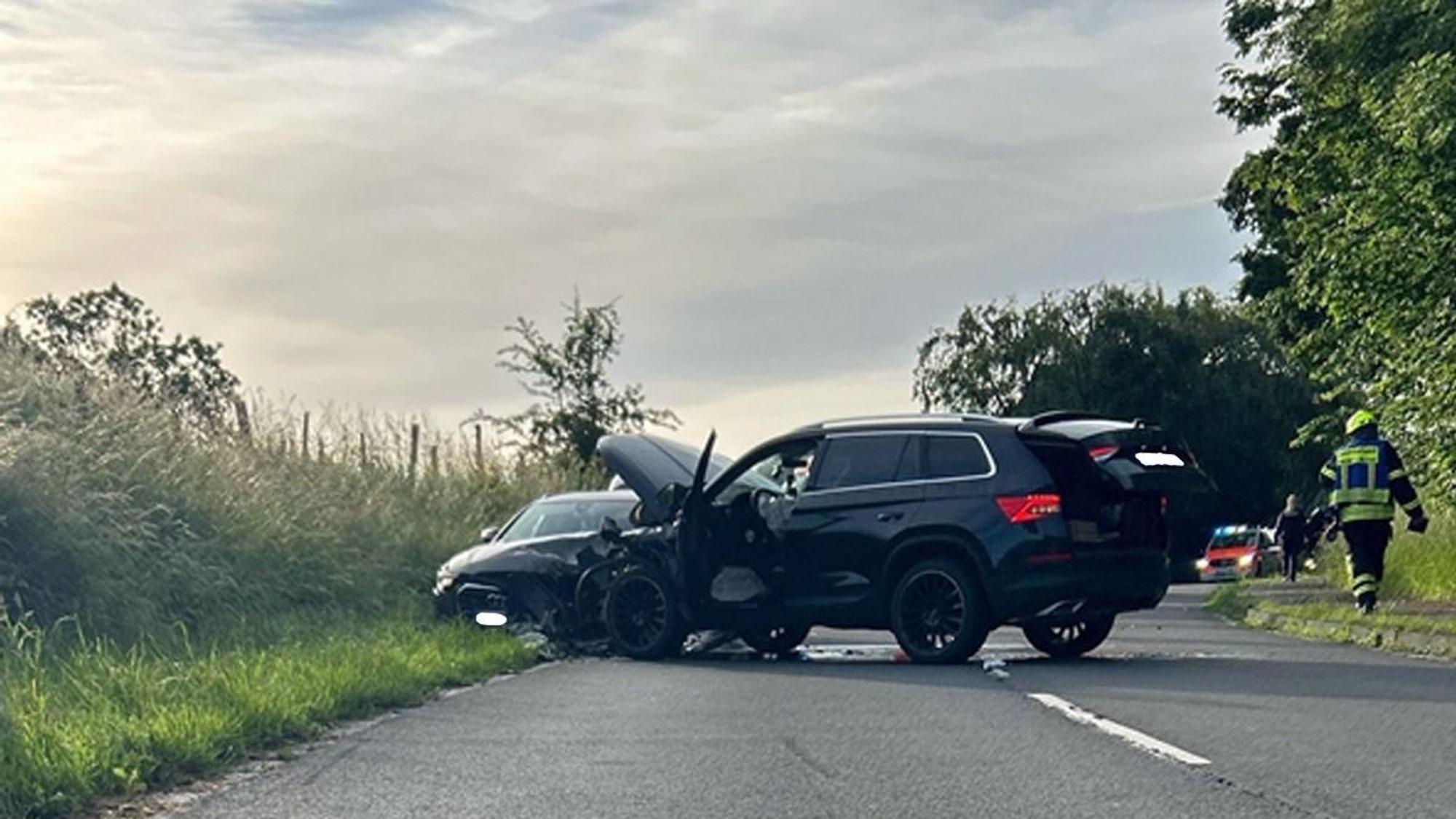 Ein verunfalltes Auto steht am Straßenrand, im Hintergrund ein Polizeiwagen.