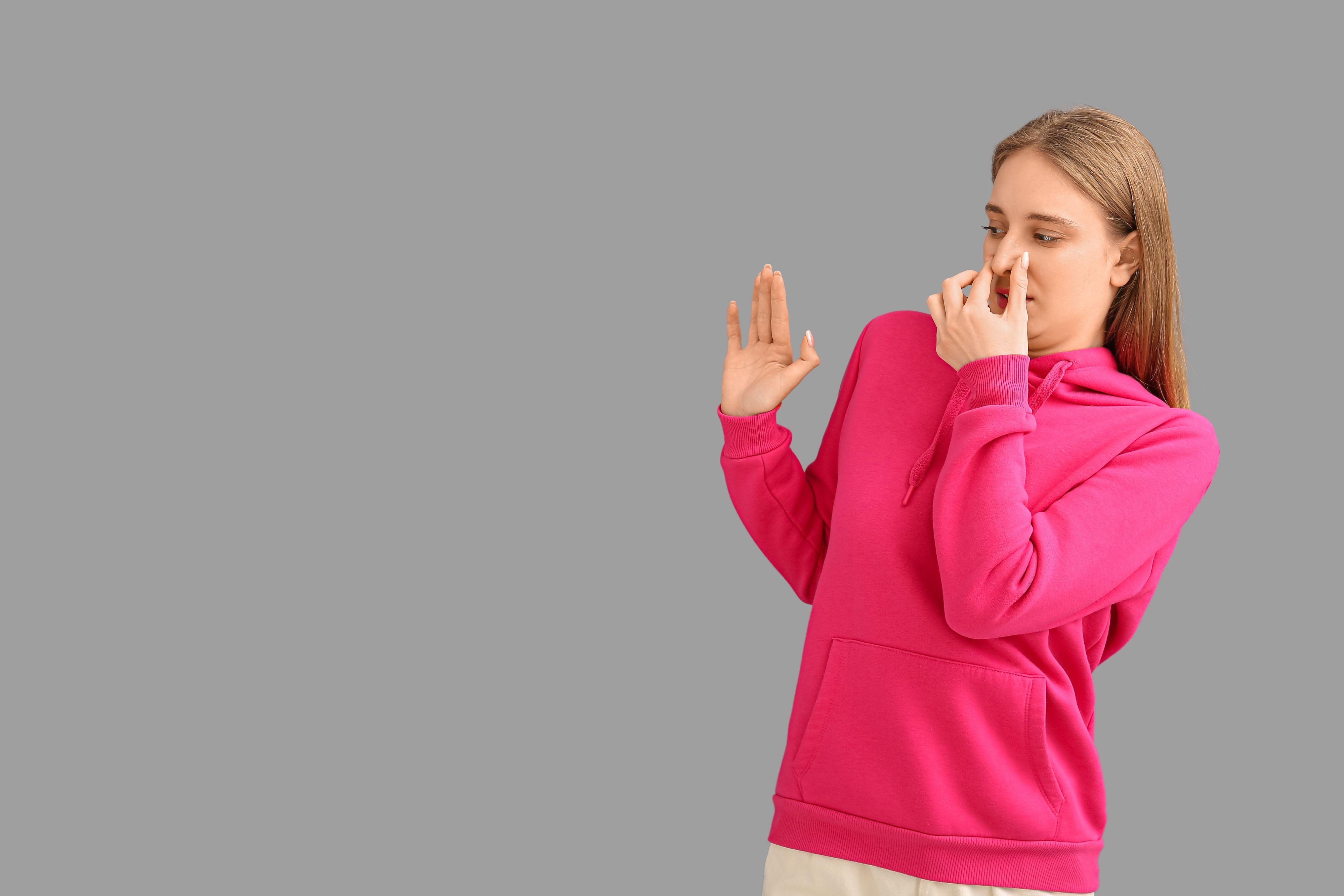 Eine Frau in einem pinken Hoodie hält sich angewidert die Nase zu