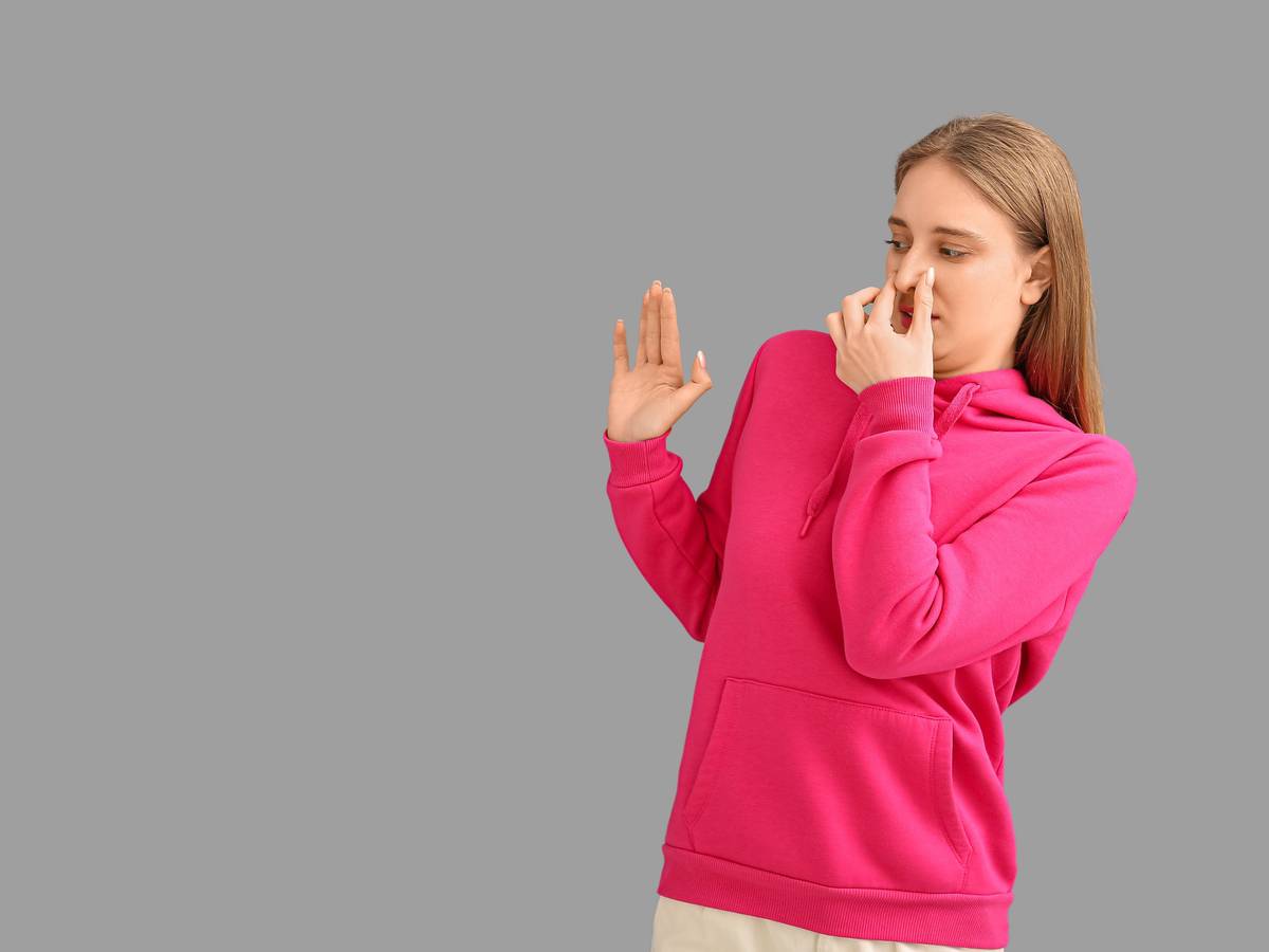 Eine Frau in einem pinken Hoodie hält sich angewidert die Nase zu