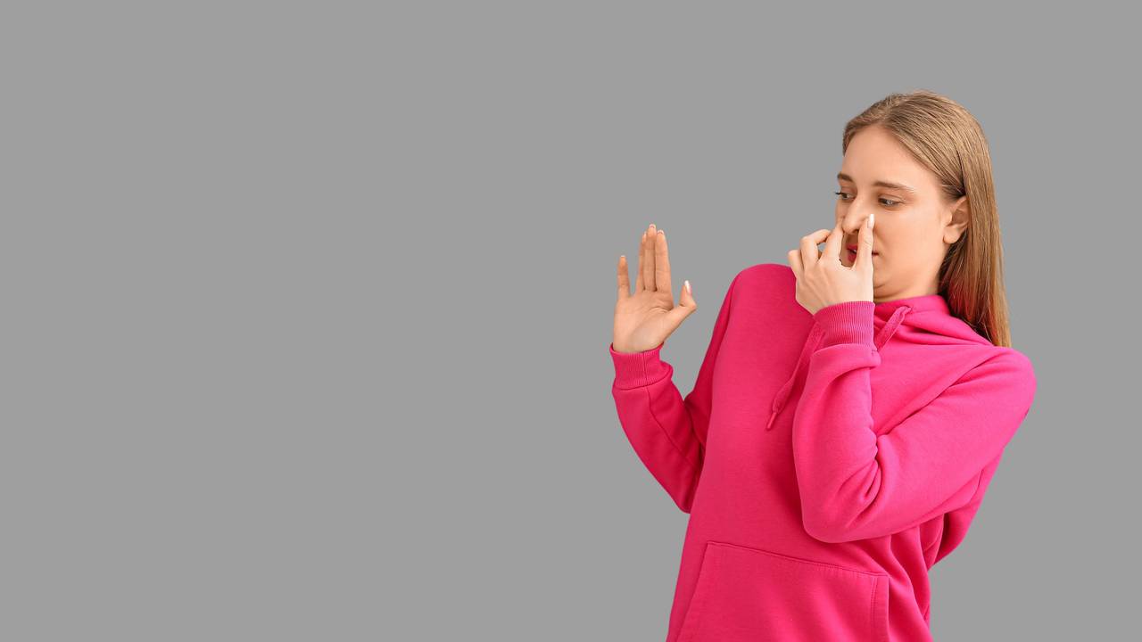 Eine Frau in einem pinken Hoodie hält sich angewidert die Nase zu