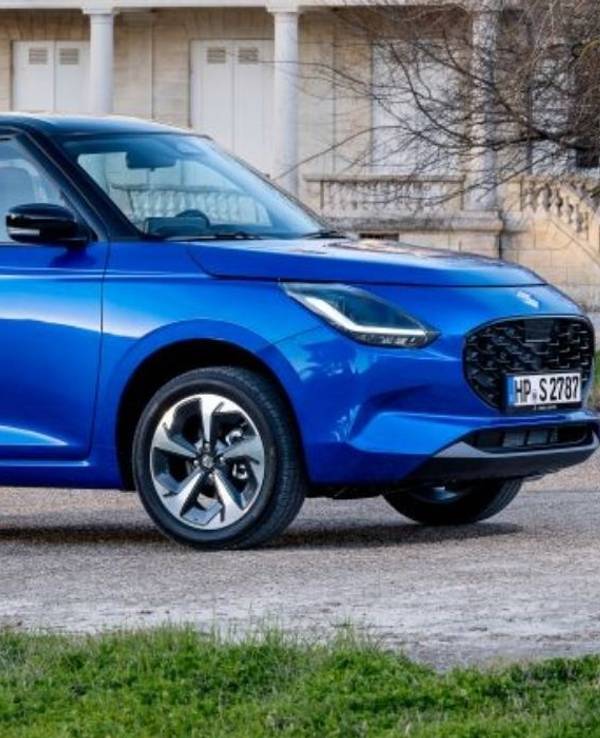 Suzuki Swift 1.2 Club in Blau steht vor einem schönen Anwesen in der Abendsonne.