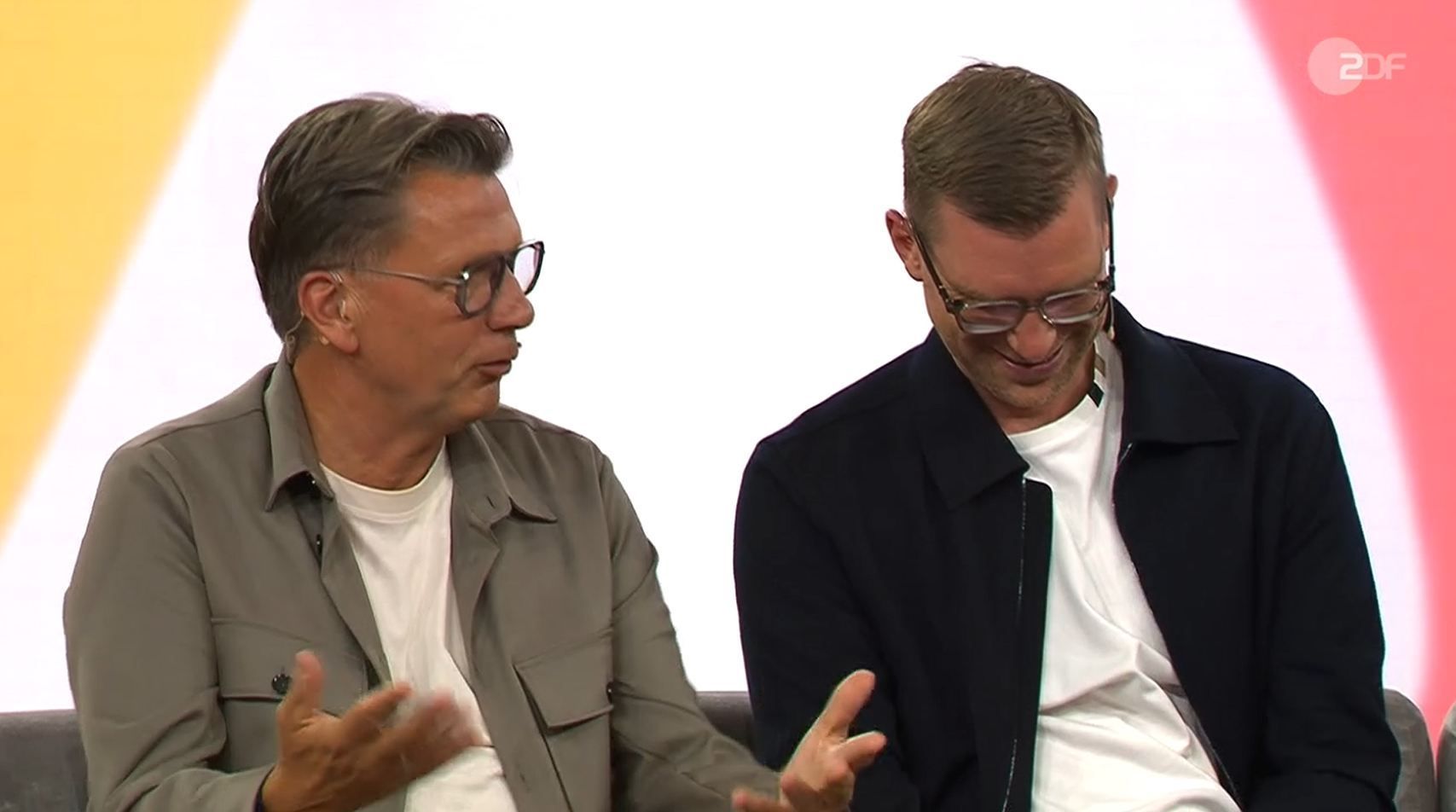 Thorsten Kinhöfer sitzt neben Per Mertesacker und gestikuliert.