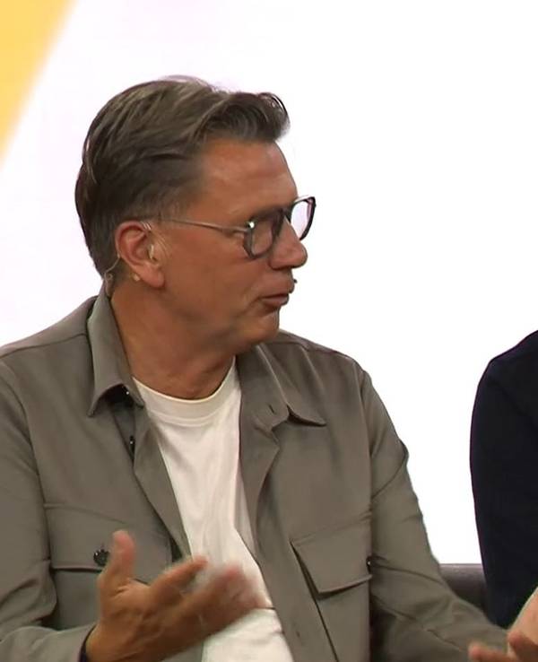 Thorsten Kinhöfer sitzt neben Per Mertesacker und gestikuliert.