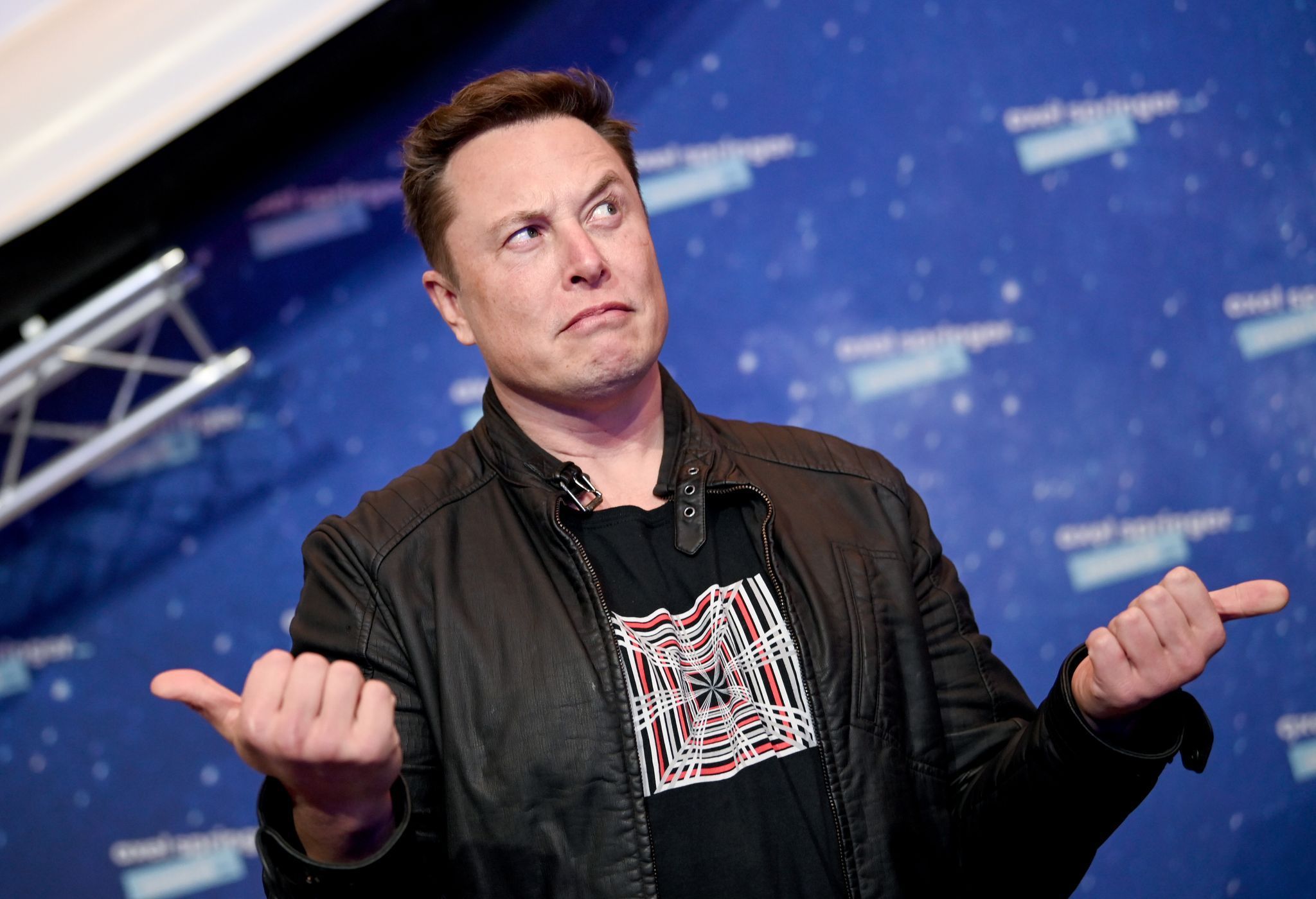 Elon Musk, Chef von SpaceX, guckt fragend vor einer Fotowand