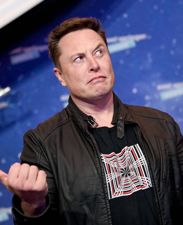 Elon Musk, Chef von SpaceX, guckt fragend vor einer Fotowand