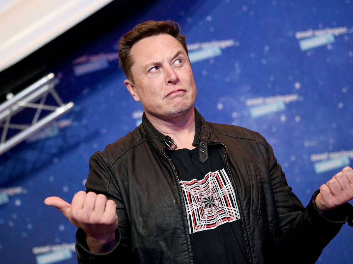 Elon Musk, Chef von SpaceX, guckt fragend vor einer Fotowand
