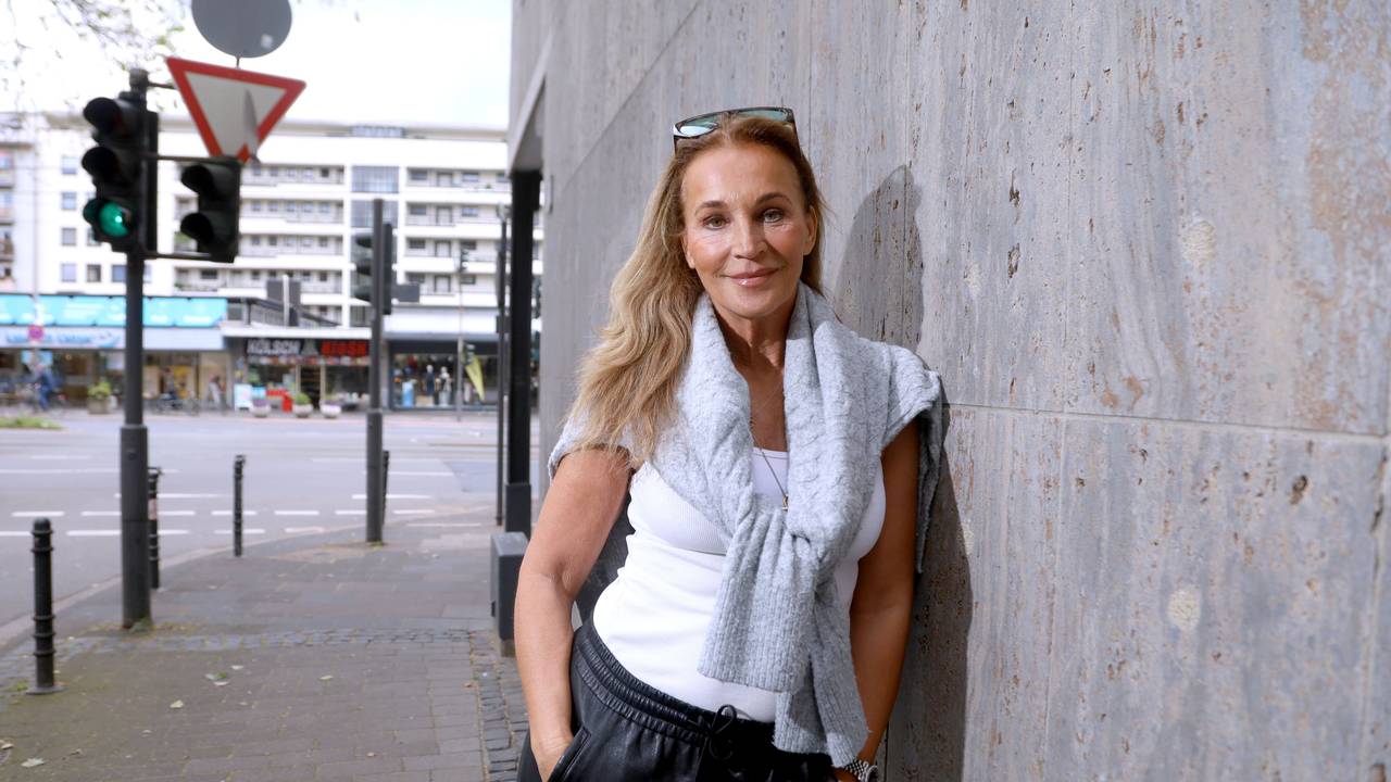 Eine Frau in lockerer Sportkleidung mit Sonnenbrille im Haaar lehnt lässig an einer Mauer