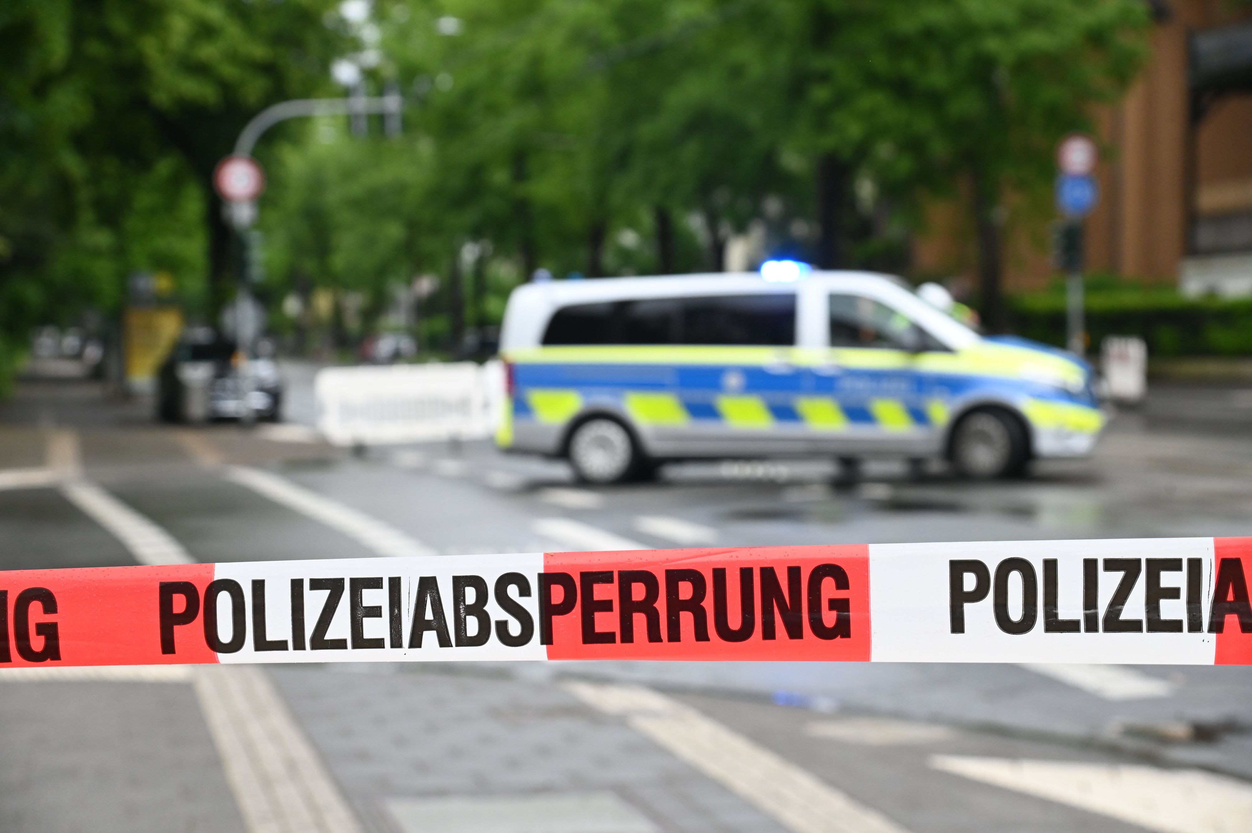 Die Polizei hat eine Straße mit Flatterband abgesperrt, im Hintergrund steht ein Polizeifahrzeug.
