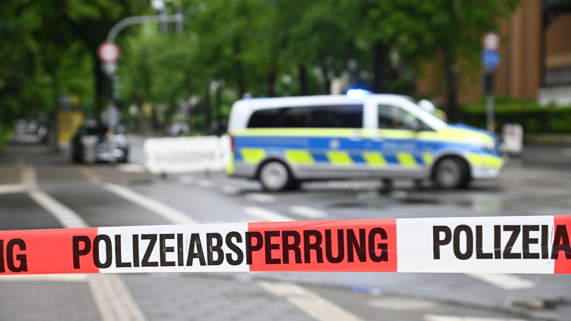Die Polizei hat eine Straße mit Flatterband abgesperrt, im Hintergrund steht ein Polizeifahrzeug.