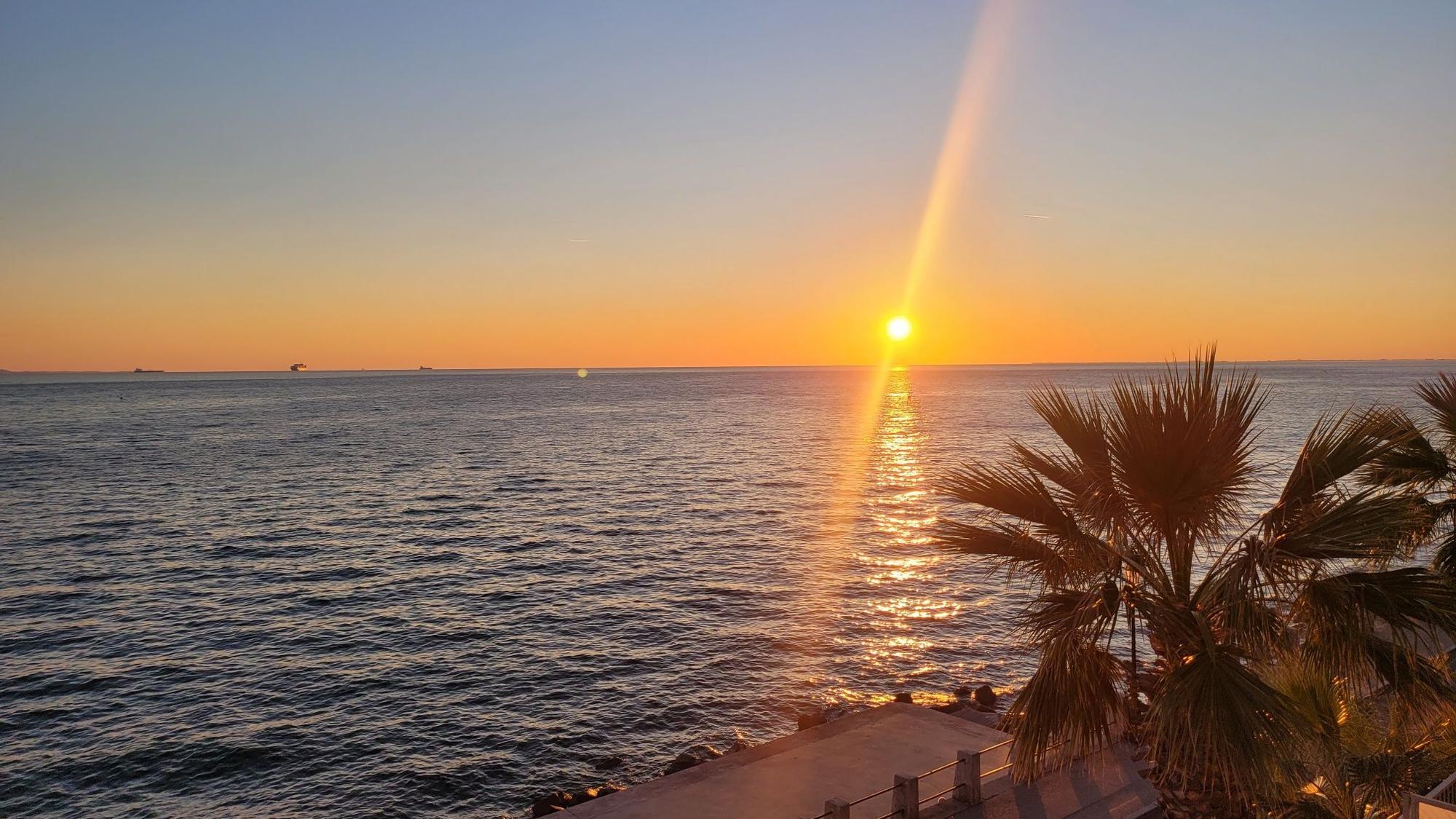 Sonnenuntergang am Meer, im Vordergrund Palmen und ein Bootsanleger.
