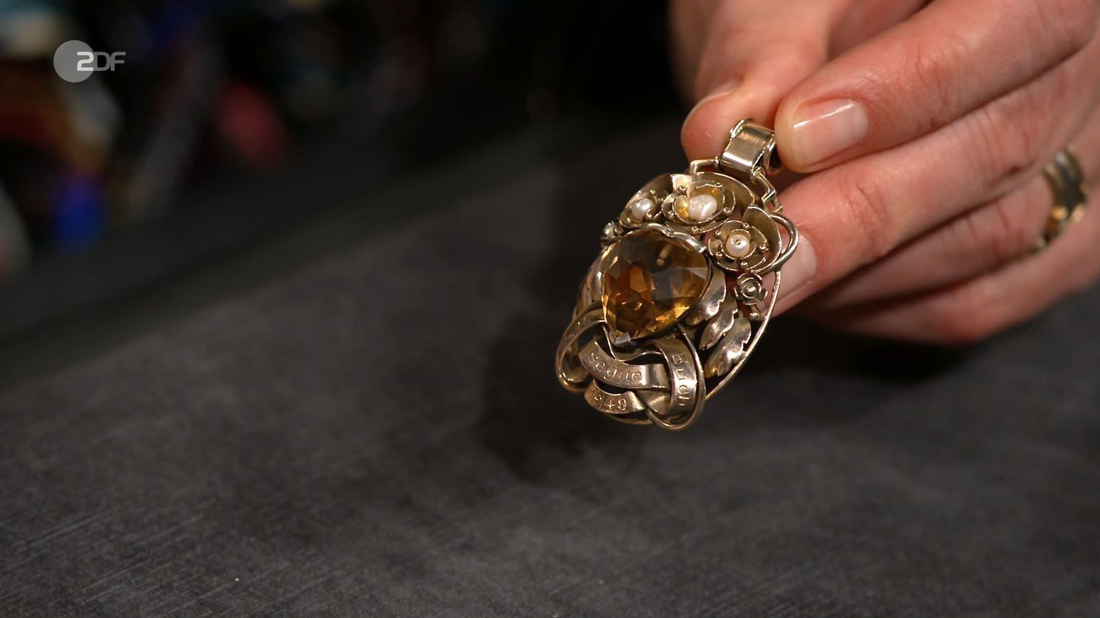 Der goldene Anhänger mit einem Citrin und der Gravur „Gott segne euch“ aus dem Jahr 1949 war 1.000 bis 1.200 Euro wert. Sarah Schreiber gab 1.300 Euro für das opulente Schmuckstück aus. 
 (Bild: ZDF)