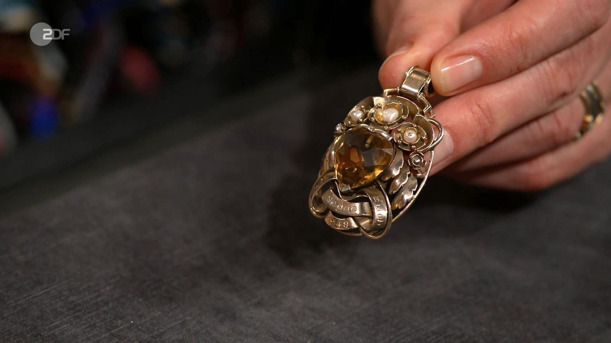 Der goldene Anhänger mit einem Citrin und der Gravur „Gott segne euch“ aus dem Jahr 1949 war 1.000 bis 1.200 Euro wert. Sarah Schreiber gab 1.300 Euro für das opulente Schmuckstück aus.
(Bild: ZDF)