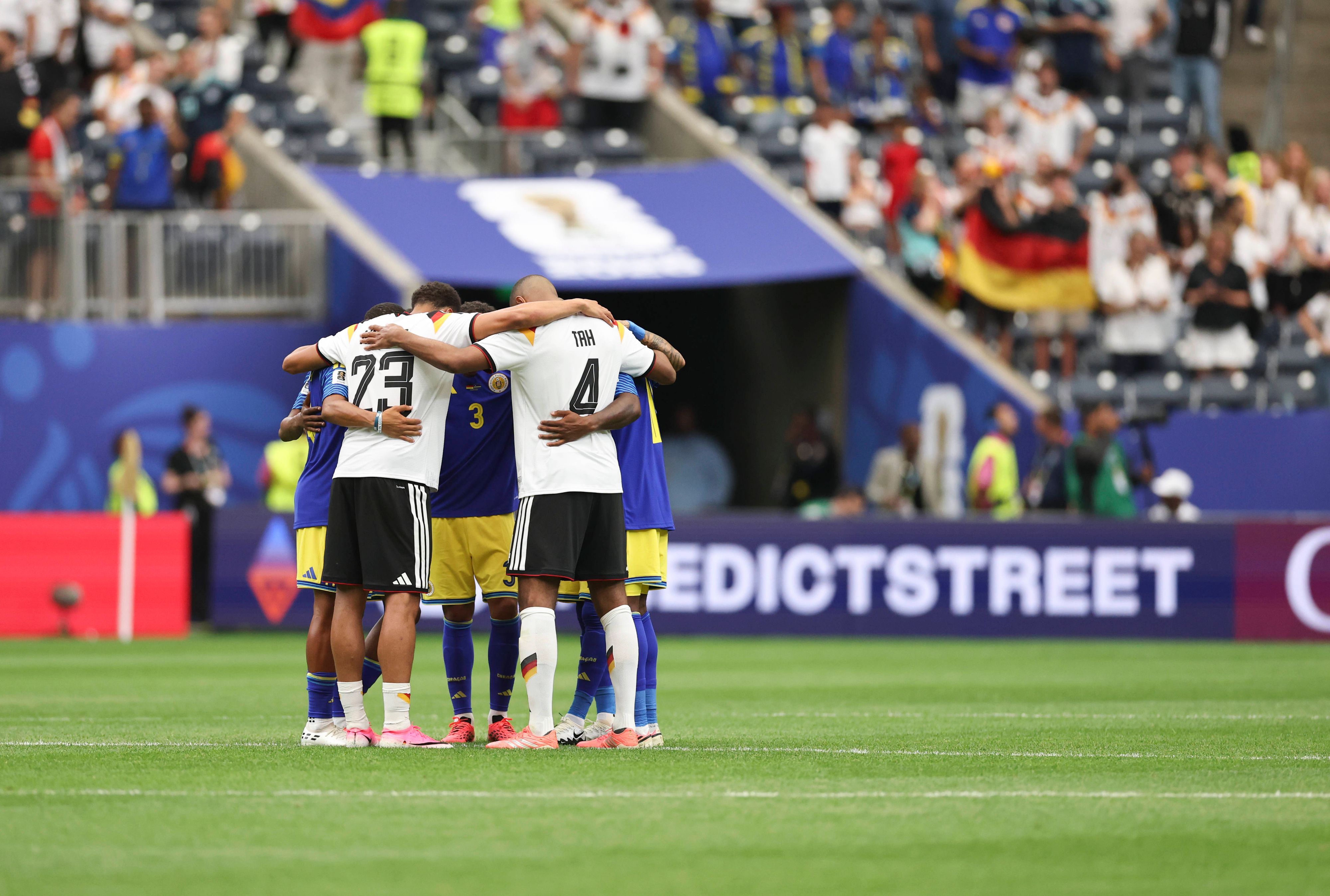 Felix Nmecha und Jonathan Tah stehen Arm in Arm mit Curacao-Spielern in einem Kreis zusammen.