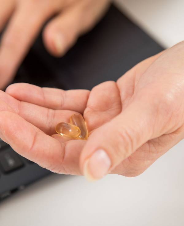 Eine Frau sitzt am Laptop und hält Kapseln in der Hand