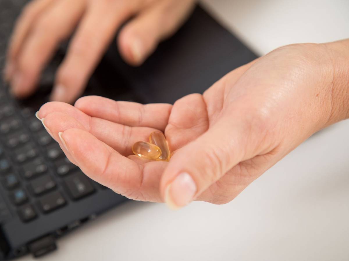 Eine Frau sitzt am Laptop und hält Kapseln in der Hand