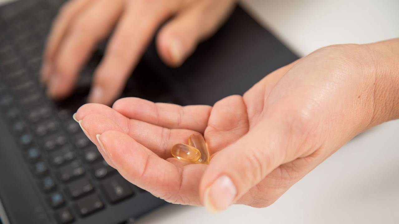 Eine Frau sitzt am Laptop und hält Kapseln in der Hand