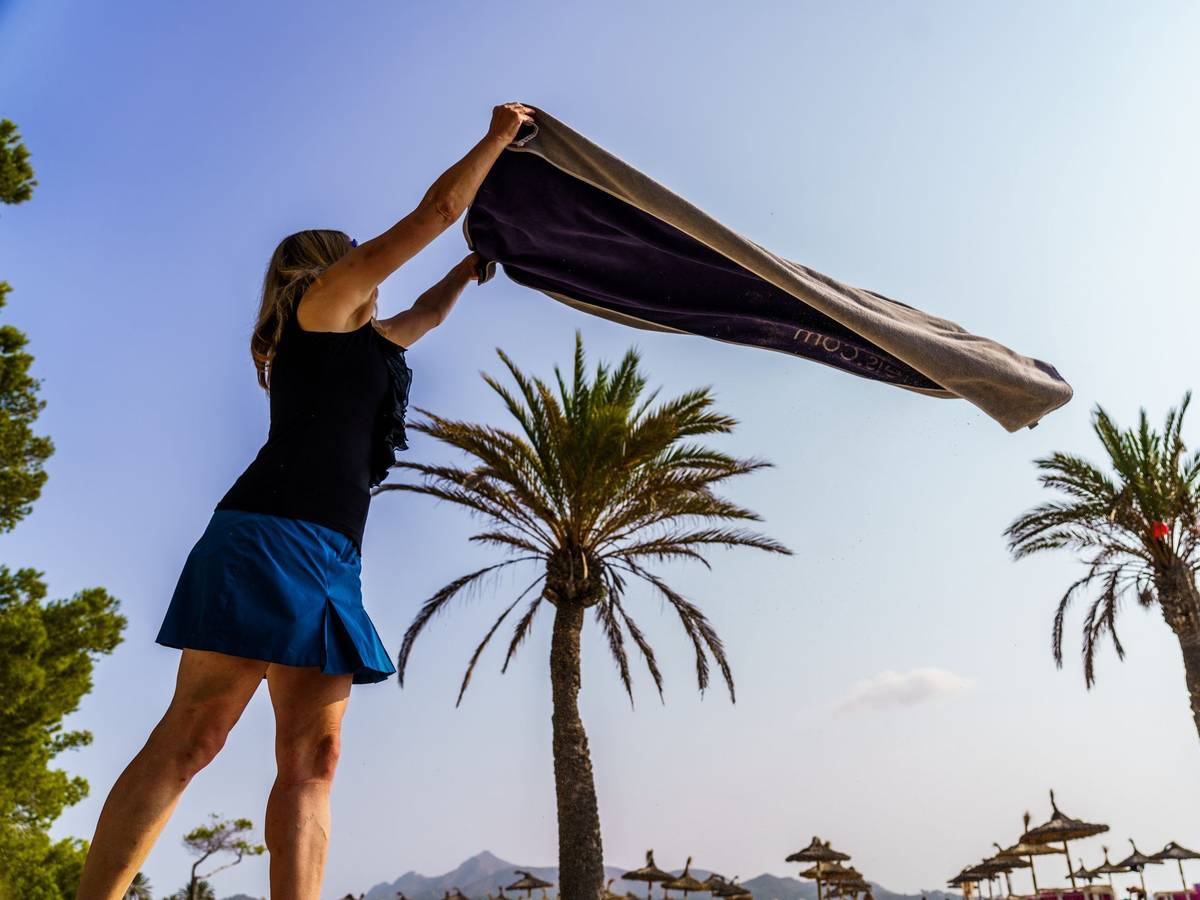 Eine Frau breitet am Strand ihr Handtuch aus