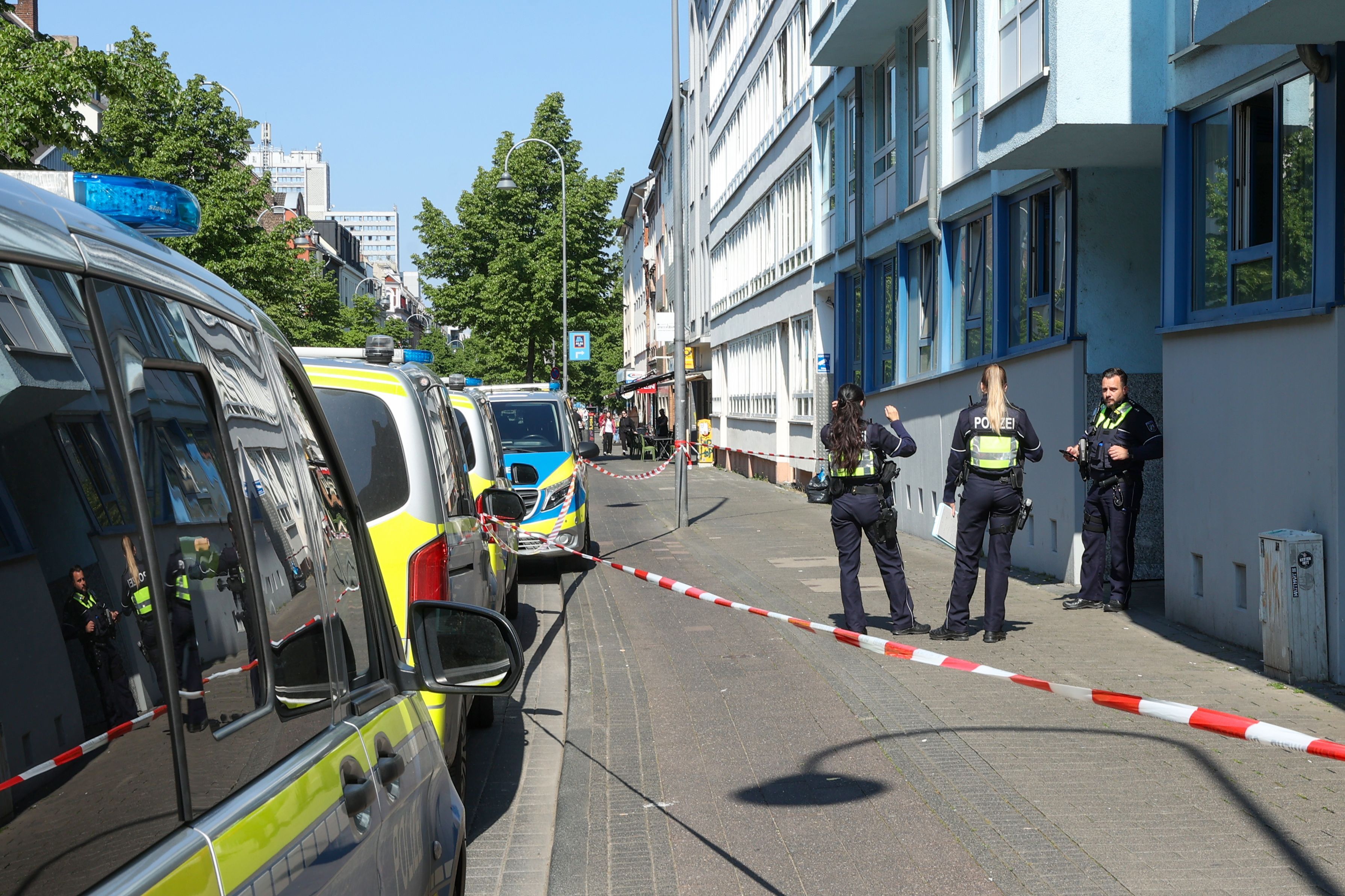 Drei Polizeikräfte stehen vor einem Haus, der Bereich davor ist mit Flatterband abgesperrt.