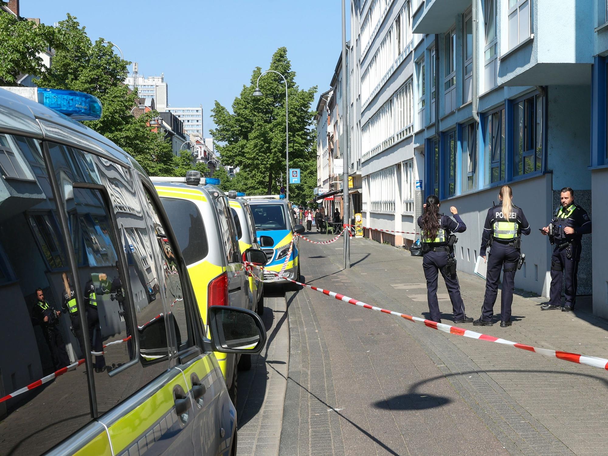 Drei Polizeikräfte stehen vor einem Haus, der Bereich davor ist mit Flatterband abgesperrt.