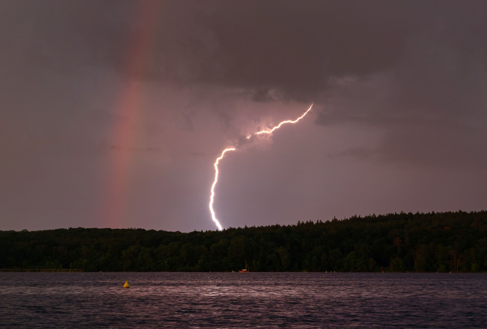 Blitz entlädt sich neben einem Regenbogen am Templiner See