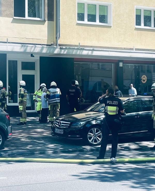 Einsatzkräfte von Feuerwehr und Polizei stehen vor einem Haus, auf der Straße liegt ein Löschschlauch.