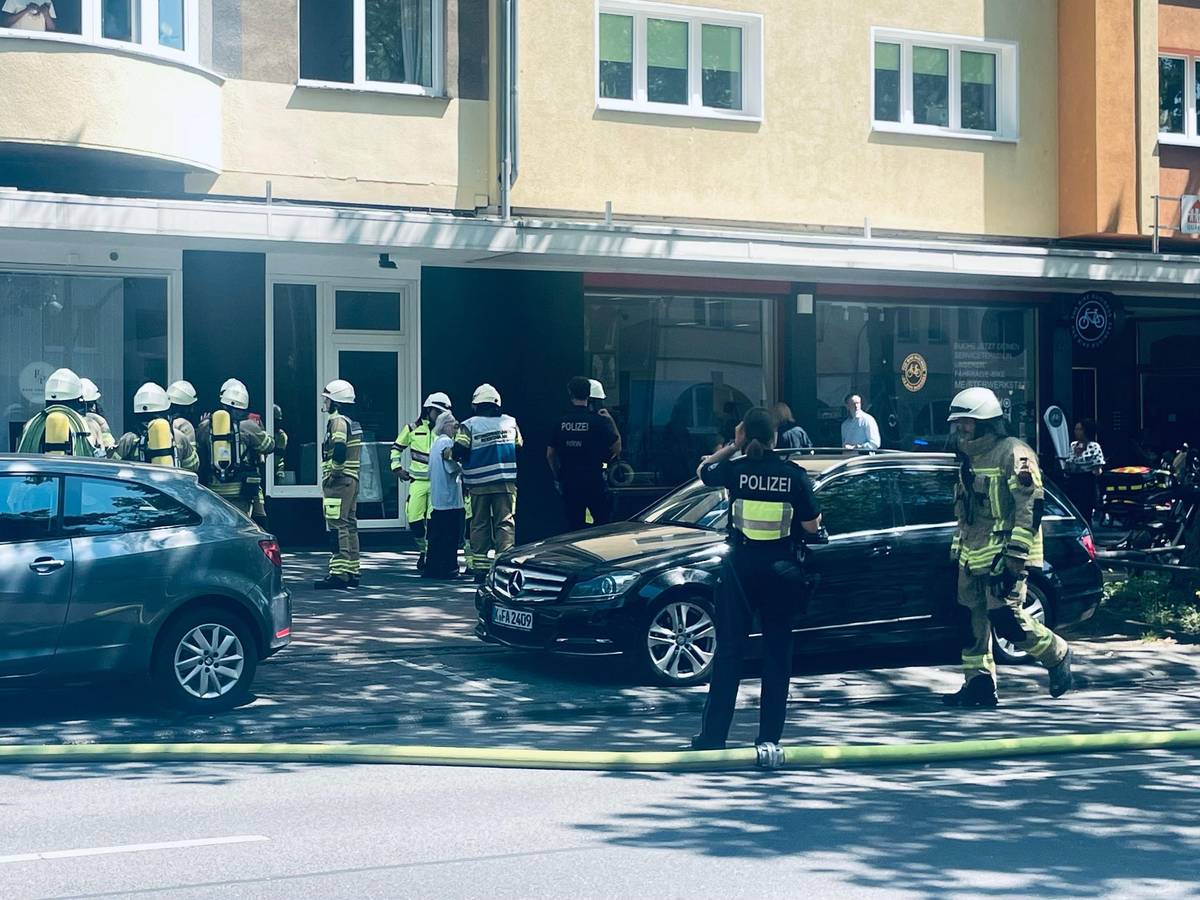 Einsatzkräfte von Feuerwehr und Polizei stehen vor einem Haus, auf der Straße liegt ein Löschschlauch.
