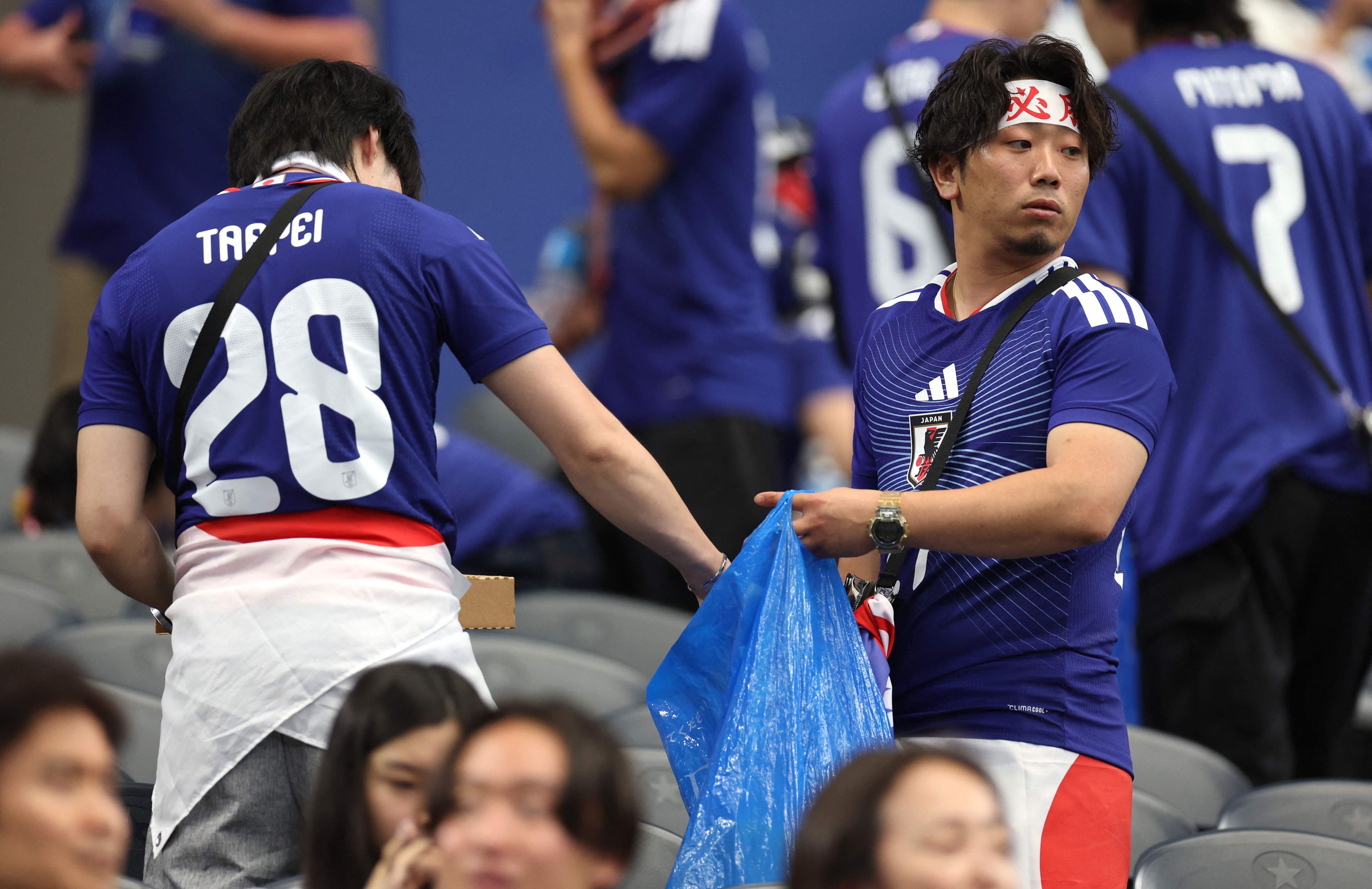 Zwei japanische Fans sammeln Müll von der Tribüne in einem blauen Müllsack.