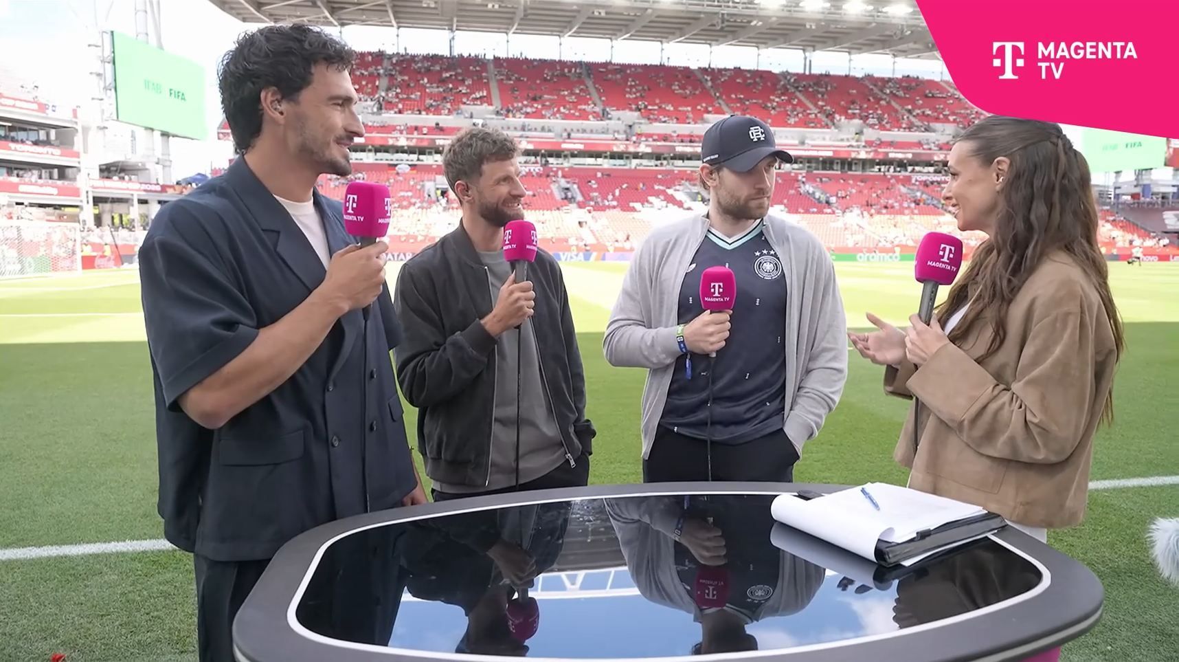Leon Draisaitl spricht mit Laura Wontorra. Thomas Müller und Mats Hummels hören zu.