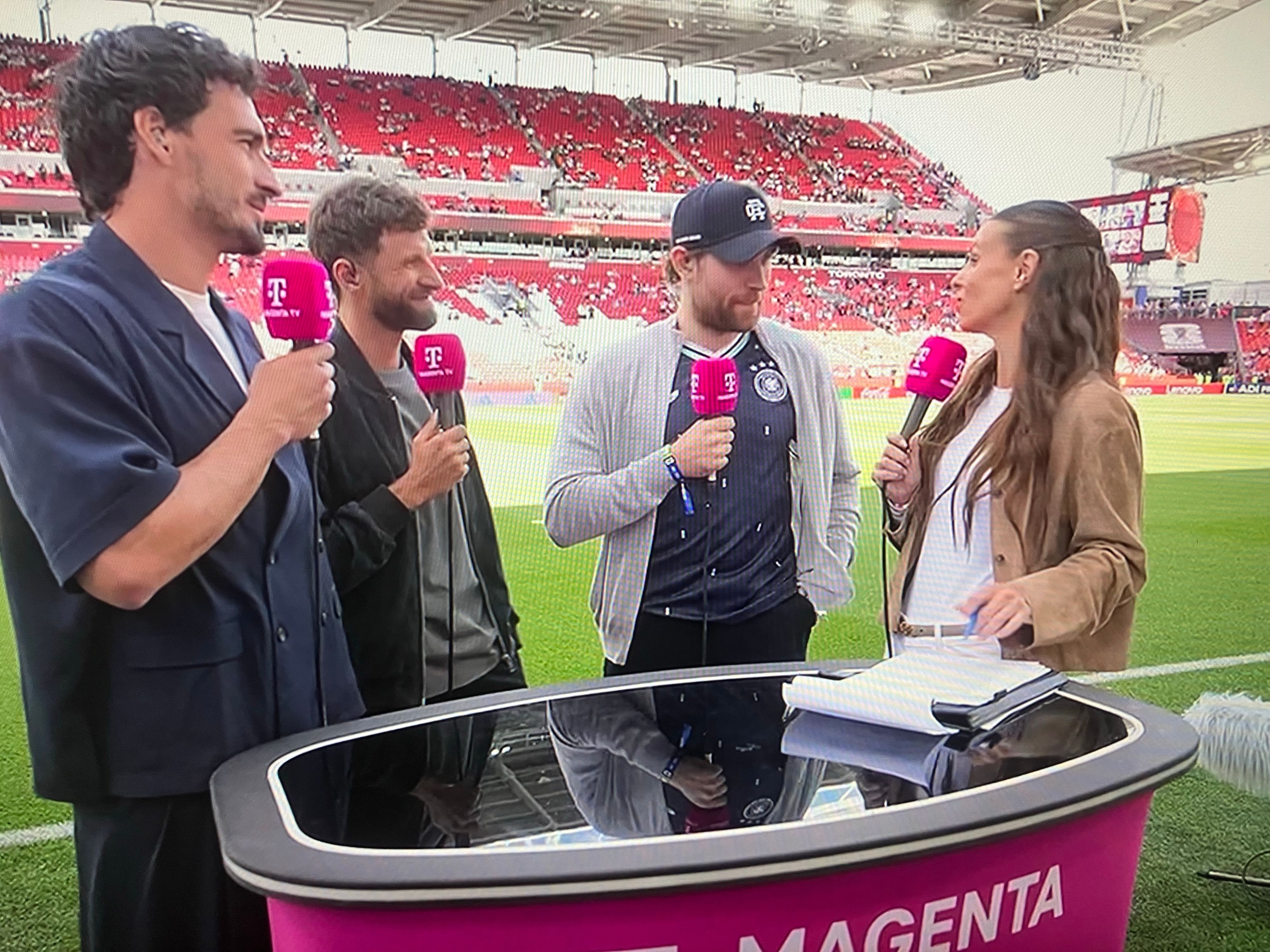 Leon Draisaitl spricht mit Laura Wontorra. Thomas Müller und Mats Hummels hören zu.