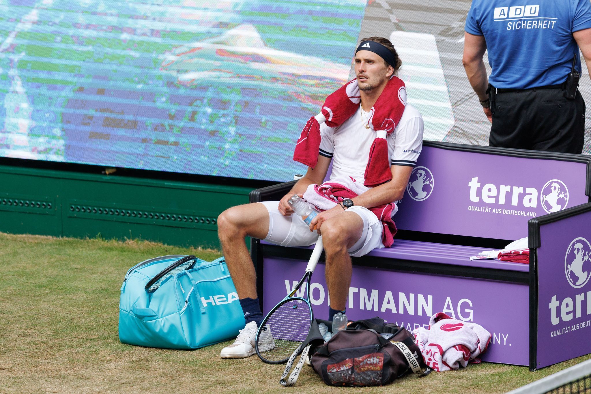 Alexander Zverev sitzt völlig fertig mit einem Kühlpad um den Hals auf der Bank beim Seitenwechsel.
