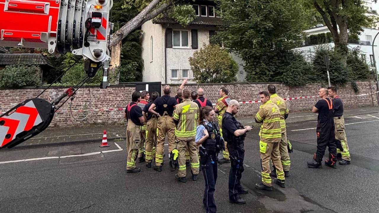 Ein Baum ist auf ein Haus gefallen, Einsatzkräfte von Feuerwehr und Polizei stehen davor