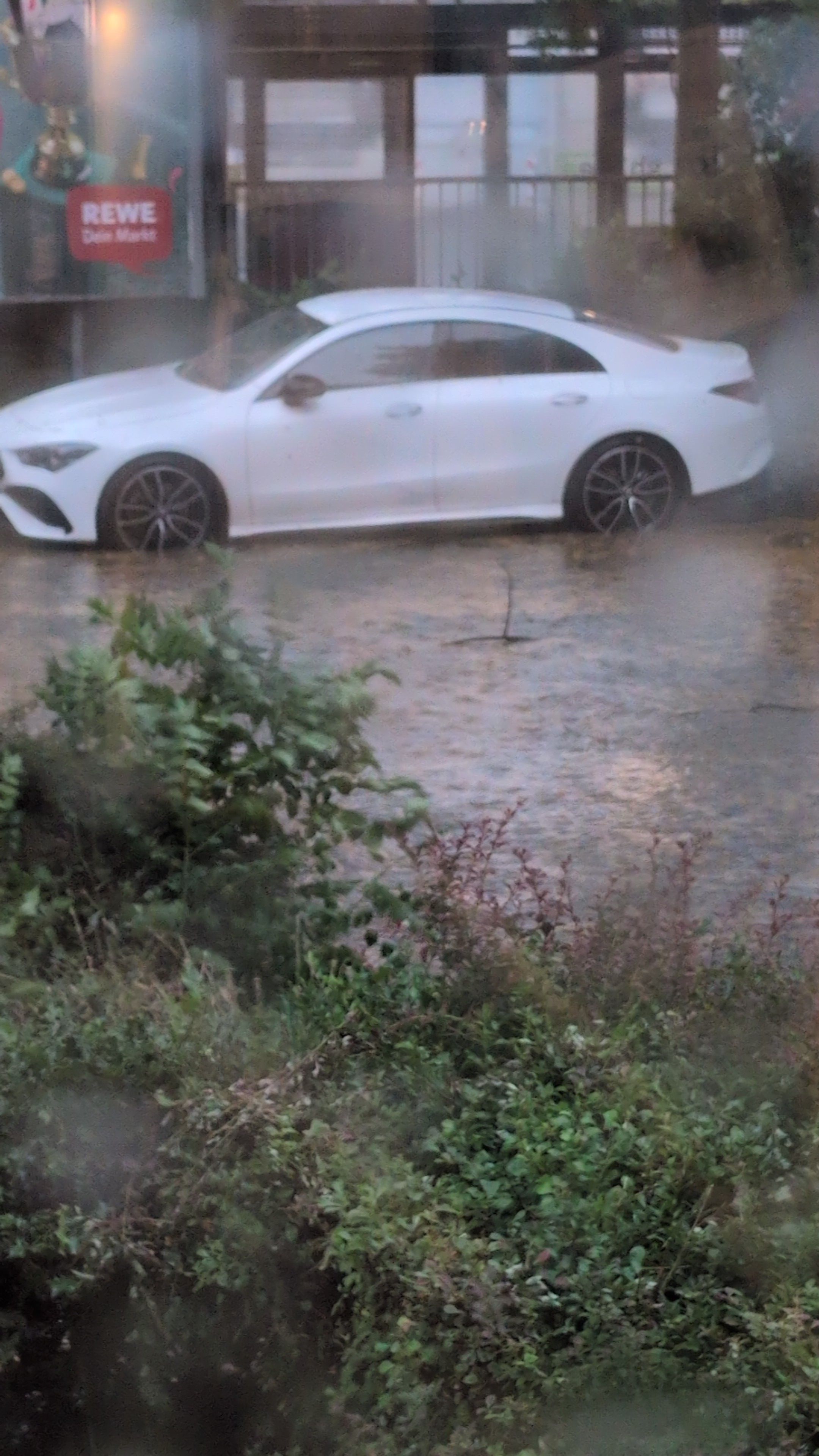 Ein Auto steht im heftigen Regen, die Straße ist überschwemmt.