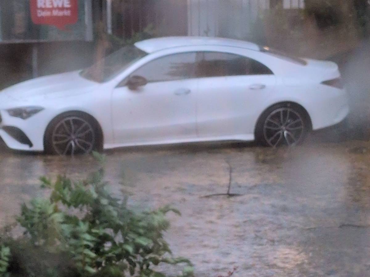 Ein Auto steht im heftigen Regen, die Straße ist überschwemmt.