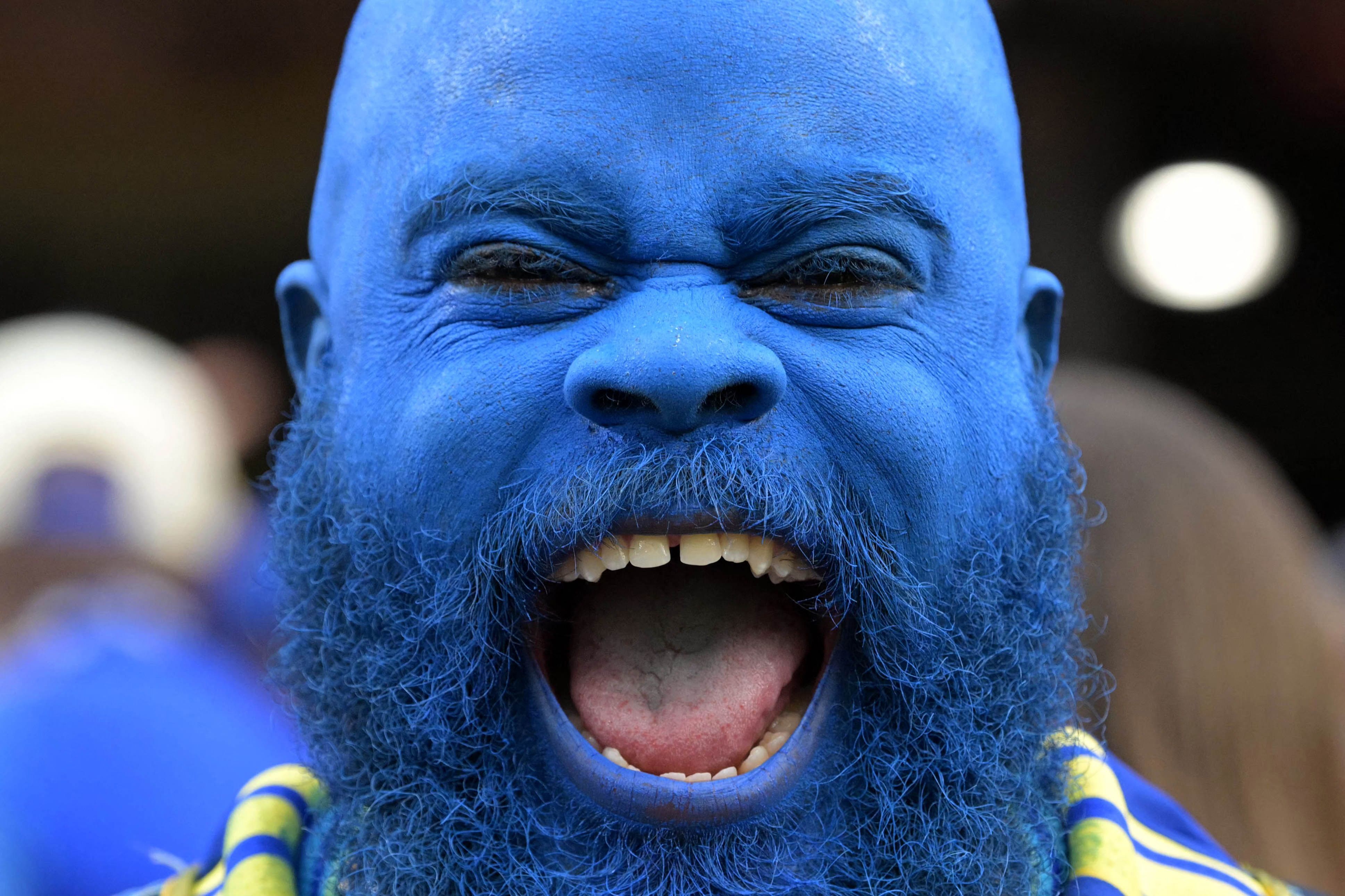 Ein Curacao-Fan, der seinen kompletten Kopf blau gefärbt hat, lacht in die Kamera.
