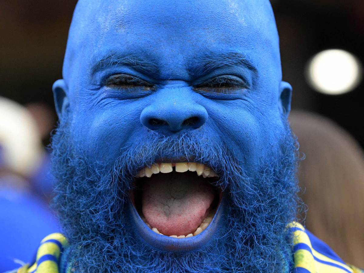 Ein Curacao-Fan, der seinen kompletten Kopf blau gefärbt hat, lacht in die Kamera.