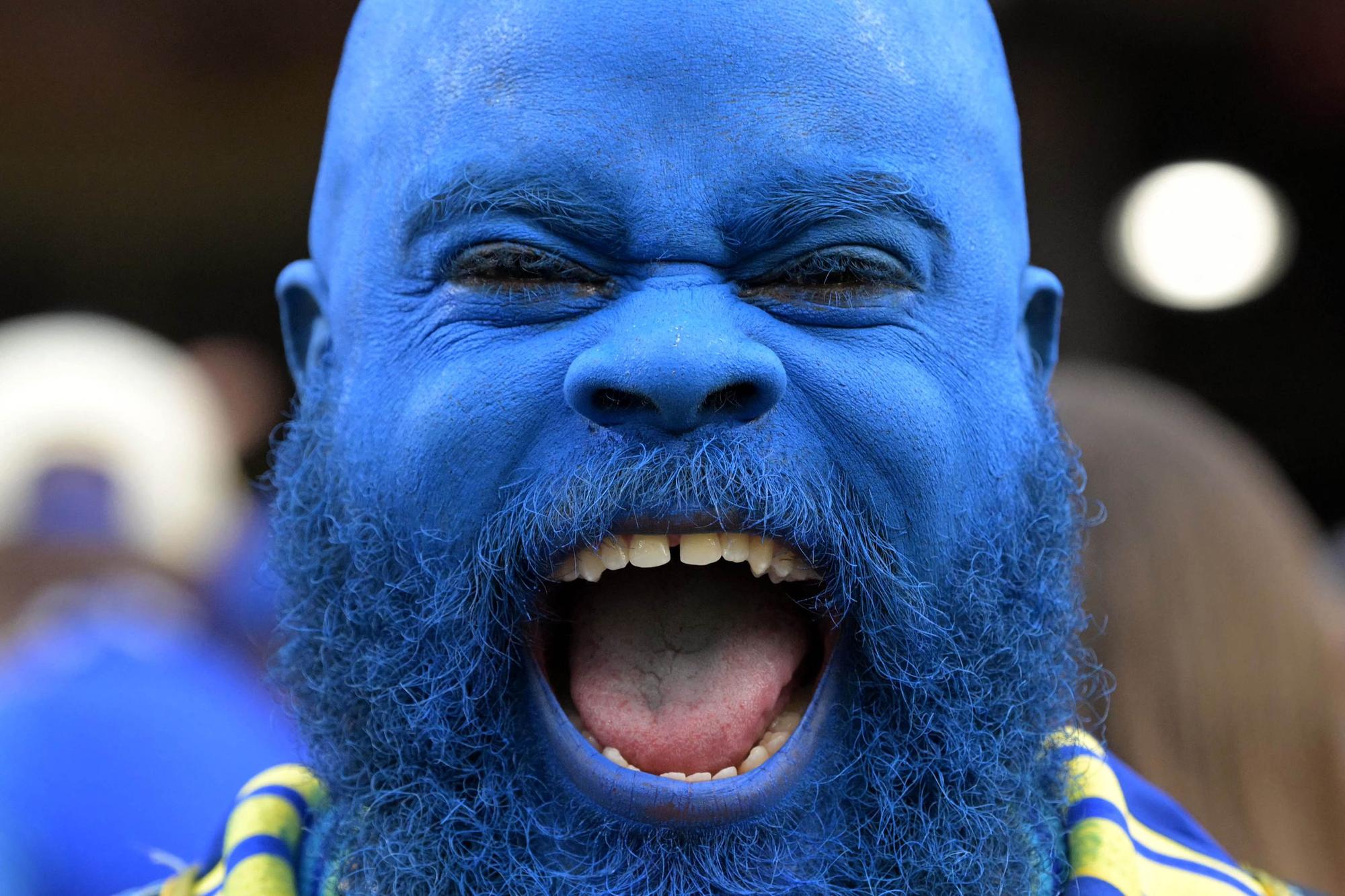 Ein Curacao-Fan, der seinen kompletten Kopf blau gefärbt hat, lacht in die Kamera.