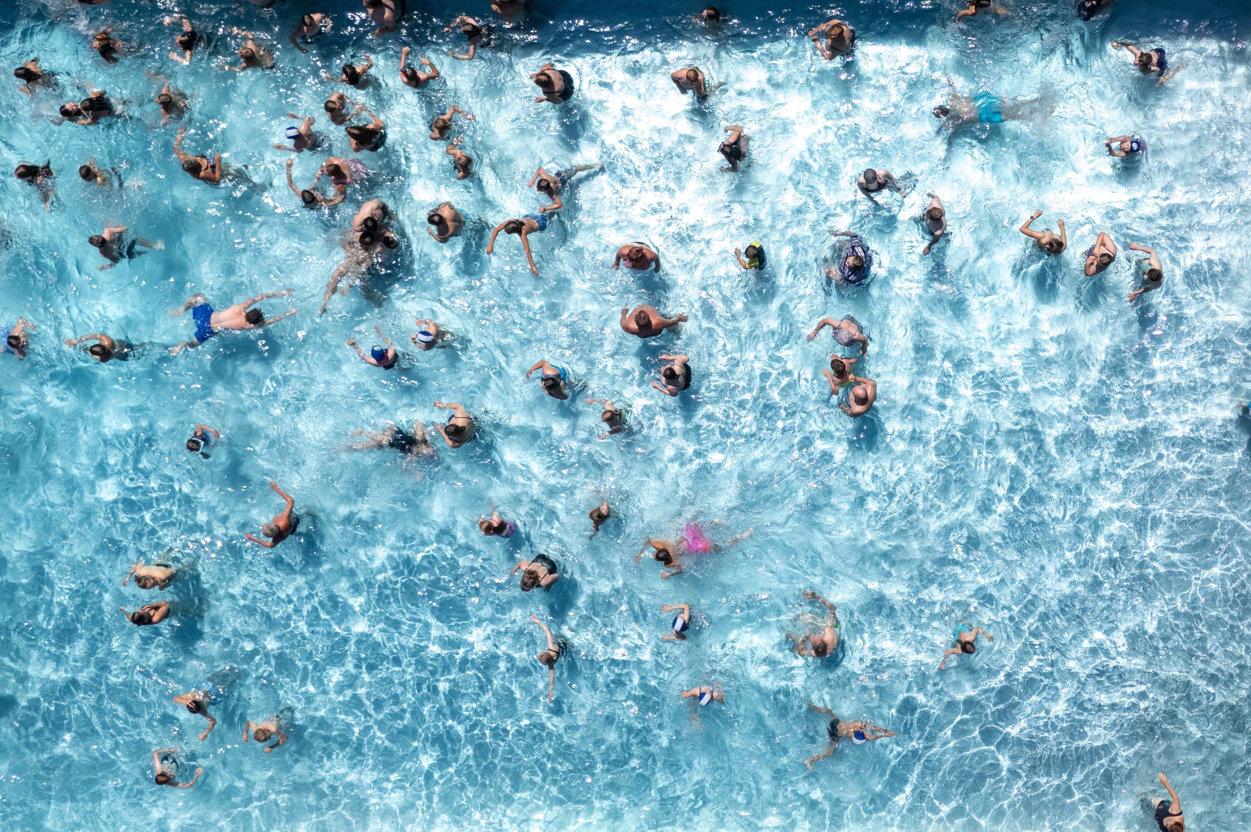Blick von oben auf ein Freibadbecken, in dessen Wasser tummeln sich zahlreiche Menschen.