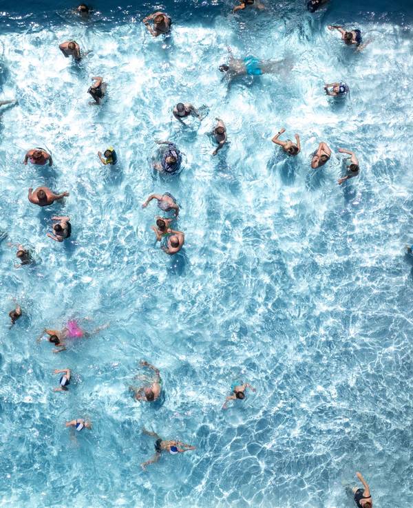 Blick von oben auf ein Freibadbecken, in dessen Wasser tummeln sich zahlreiche Menschen.