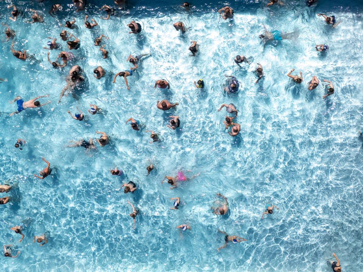 Blick von oben auf ein Freibadbecken, in dessen Wasser tummeln sich zahlreiche Menschen.