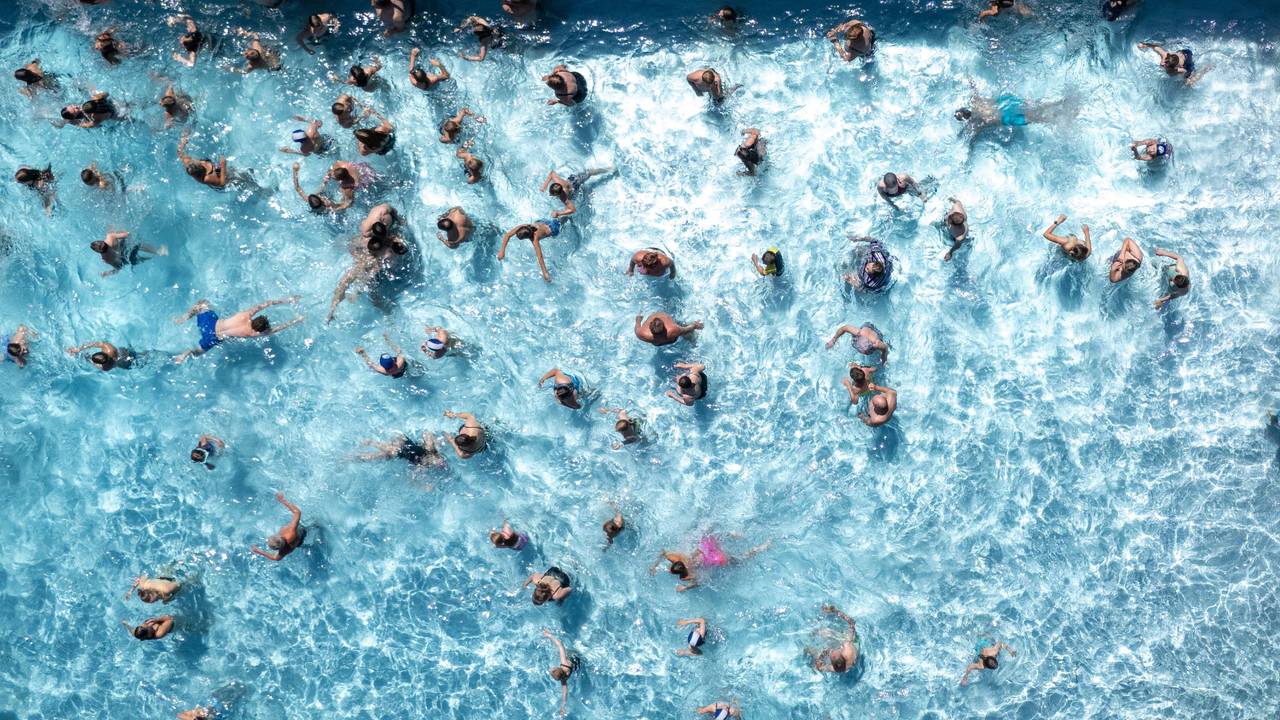 Blick von oben auf ein Freibadbecken, in dessen Wasser tummeln sich zahlreiche Menschen.