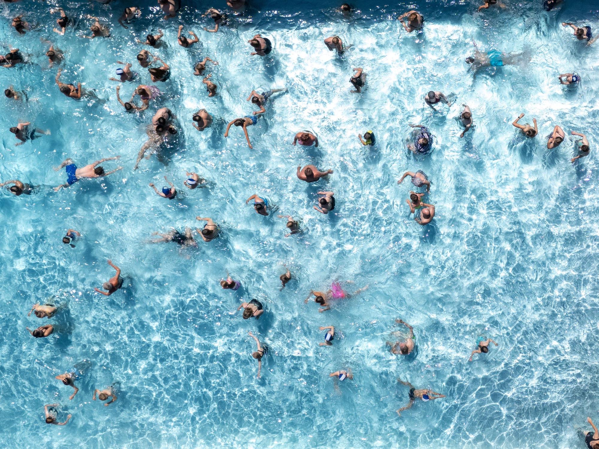 Blick von oben auf ein Freibadbecken, in dessen Wasser tummeln sich zahlreiche Menschen.