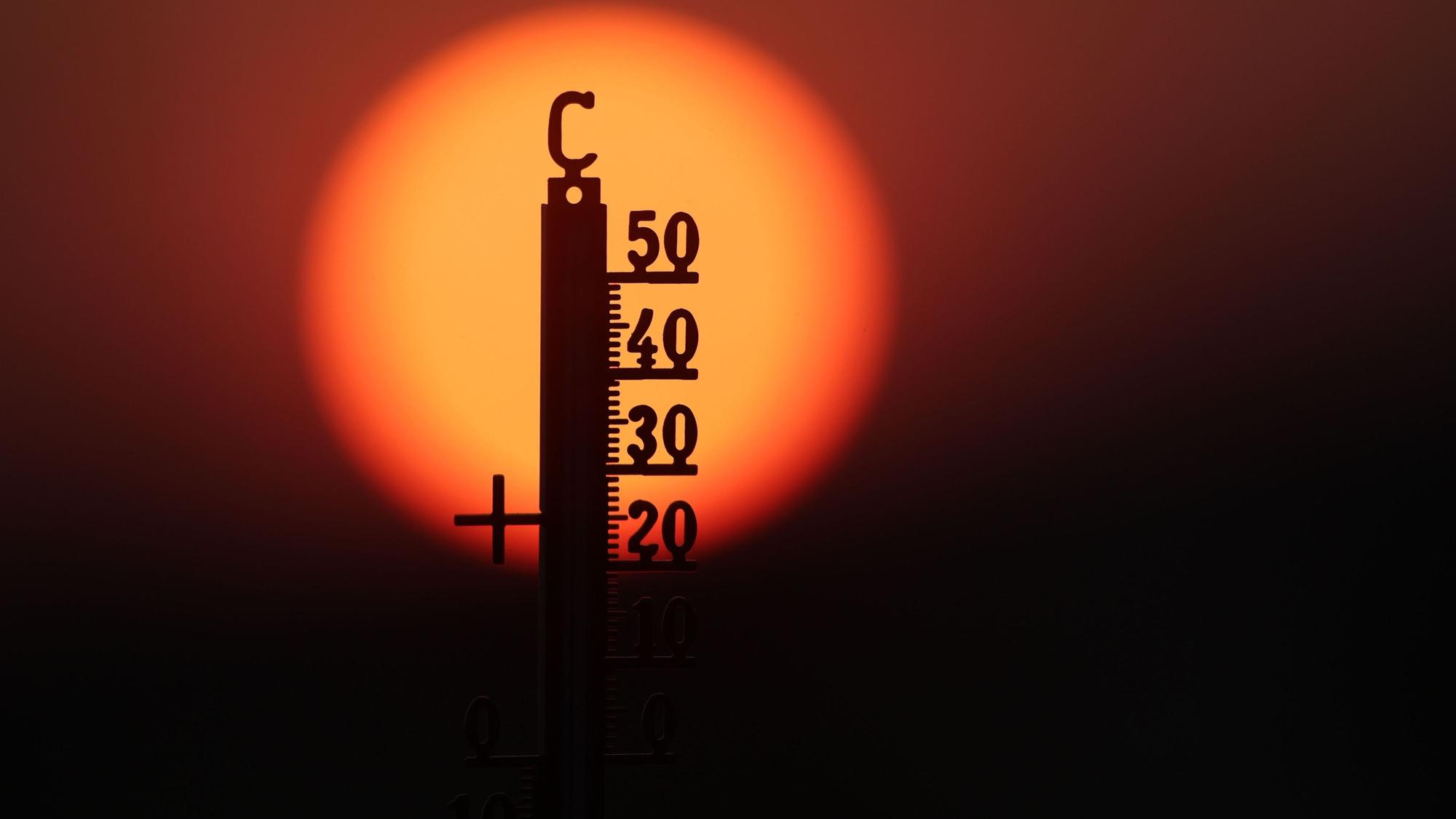 Hinter einem Thermometer geht am Morgen die Sonne auf (Illustration).