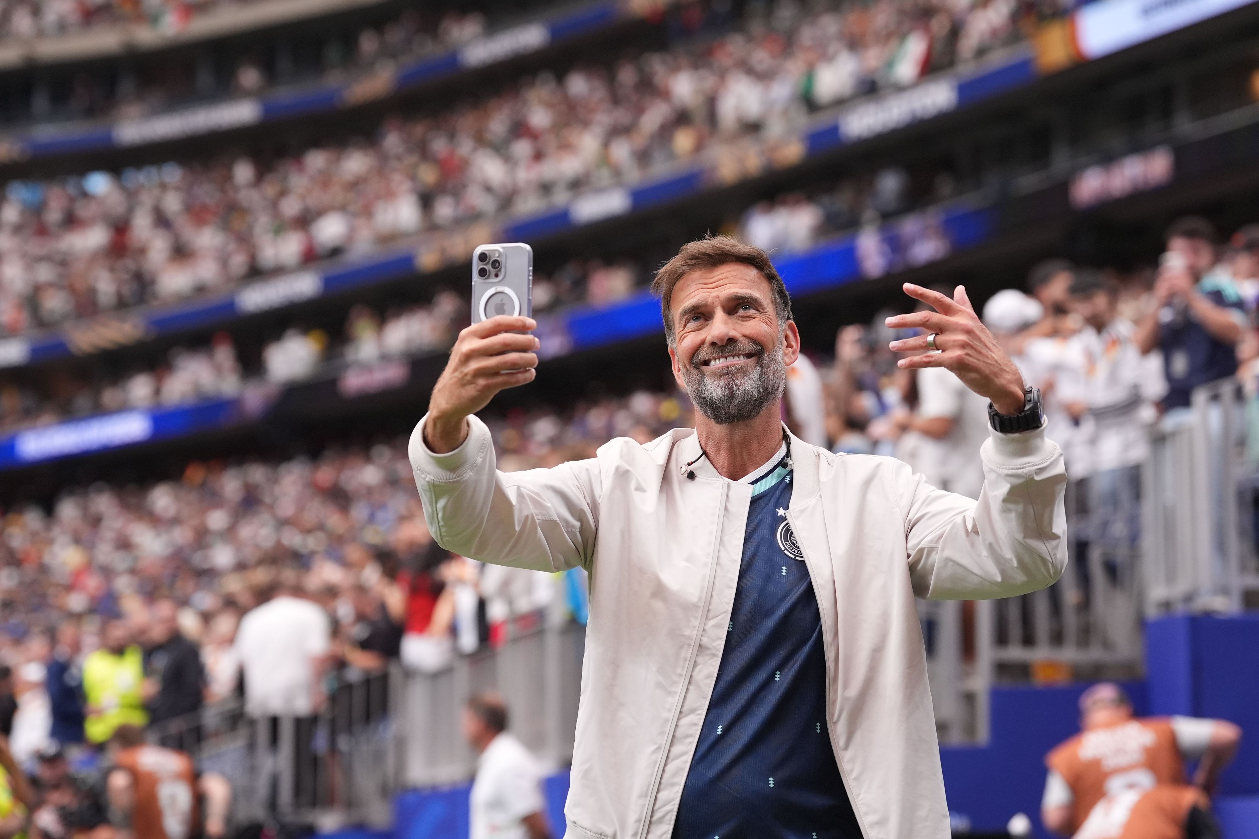 Jürgen Klopp steht im Stadion und hält ein Handy in der Hand.