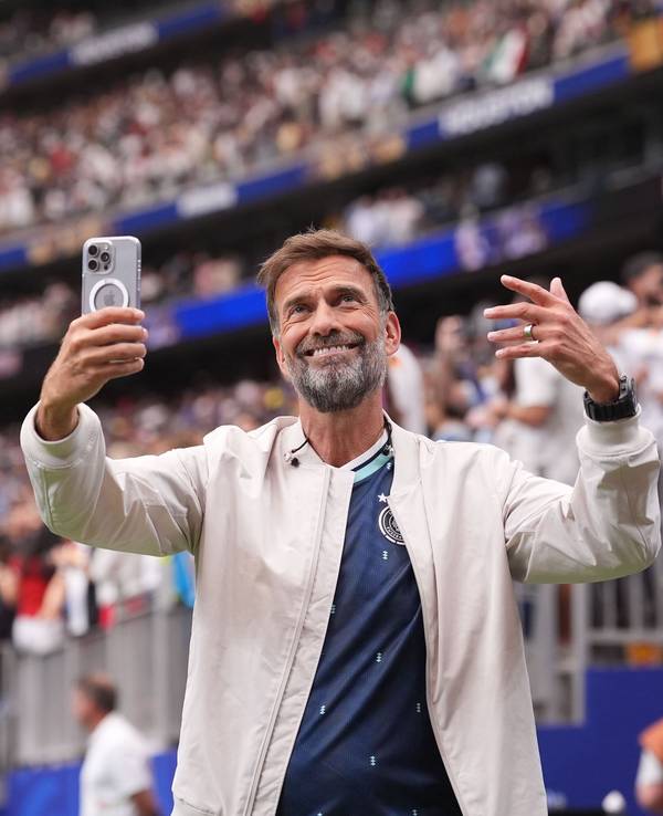 Jürgen Klopp steht im Stadion und hält ein Handy in der Hand.