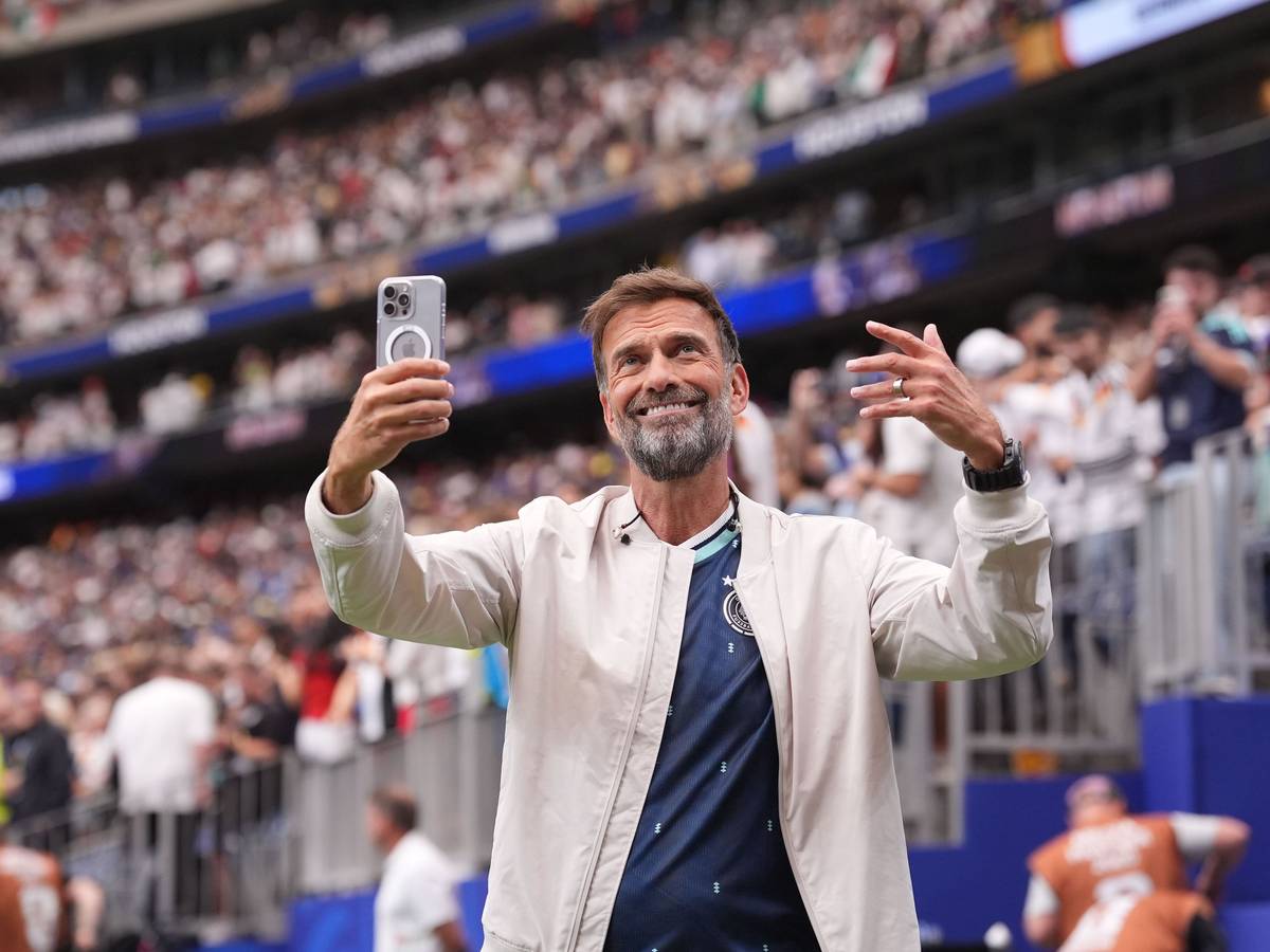 Jürgen Klopp steht im Stadion und hält ein Handy in der Hand.