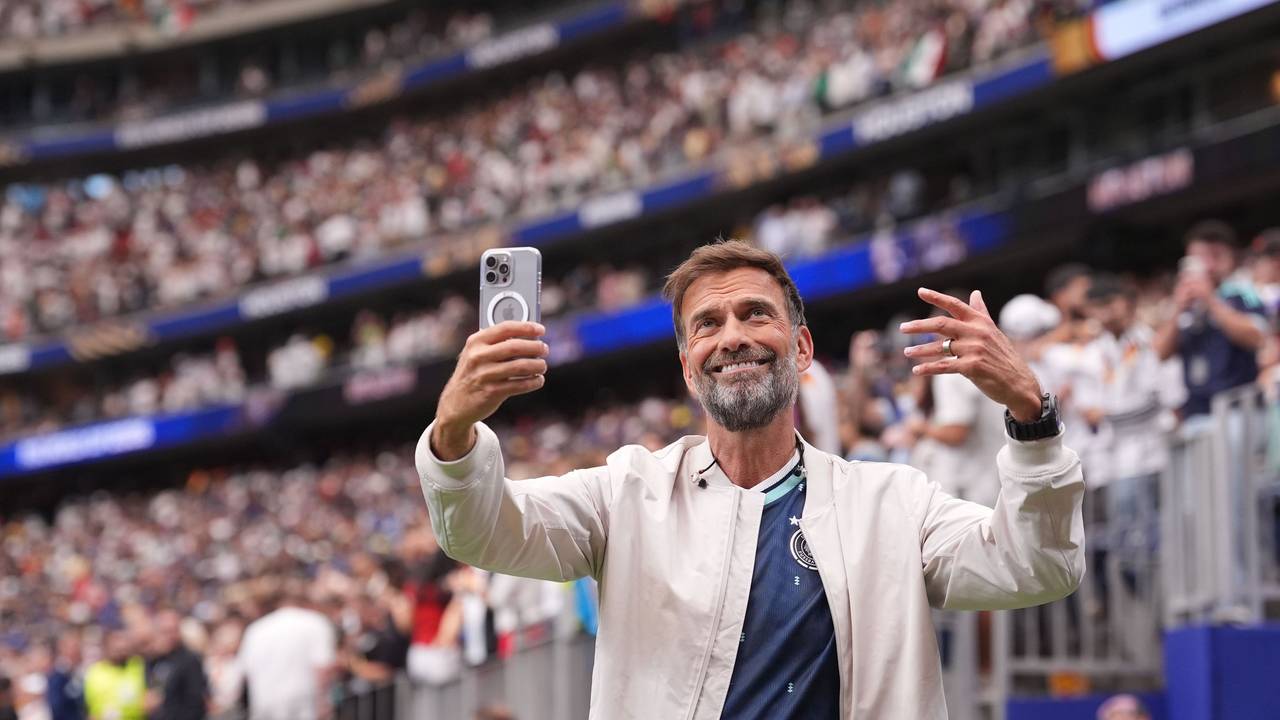 Jürgen Klopp steht im Stadion und hält ein Handy in der Hand.