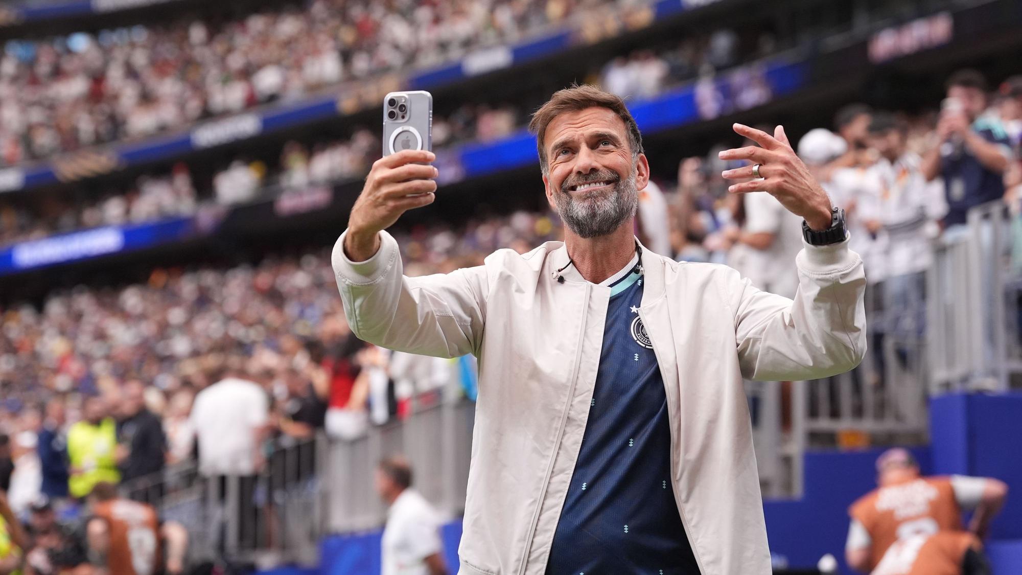 Jürgen Klopp steht im Stadion und hält ein Handy in der Hand.