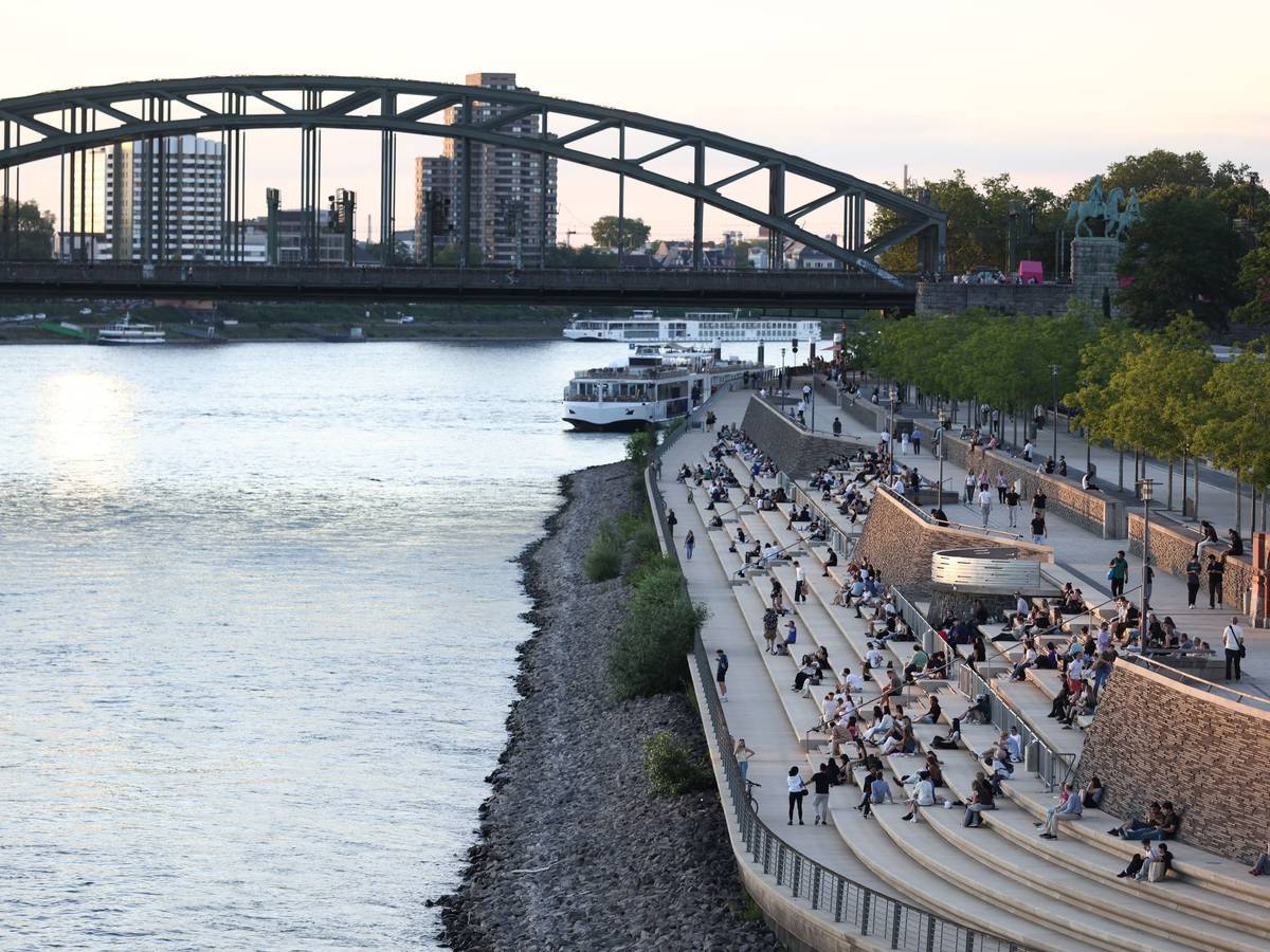 Menschen genießen bei sommerlichen Temperaturen den Blick auf Rhein und Dom am Rheinboulevard. Die Temperaturen des Flusses sind angestiegen.