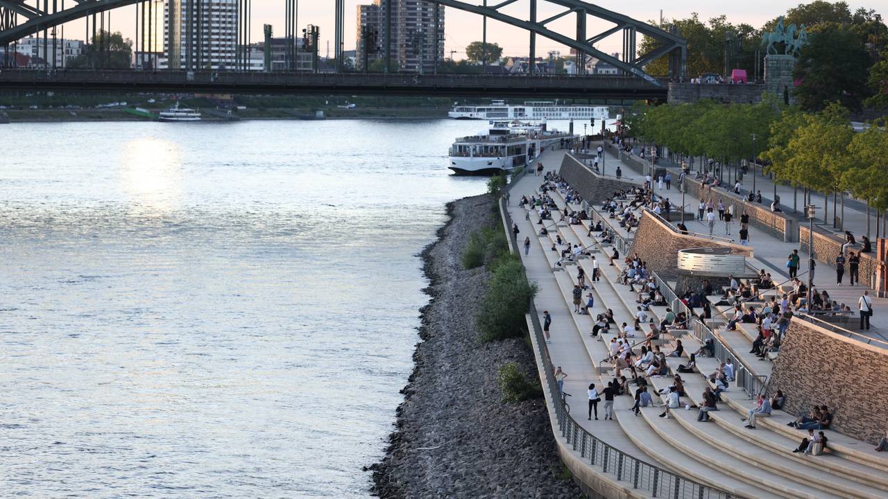 Menschen genießen bei sommerlichen Temperaturen den Blick auf Rhein und Dom am Rheinboulevard. Die Temperaturen des Flusses sind angestiegen.
