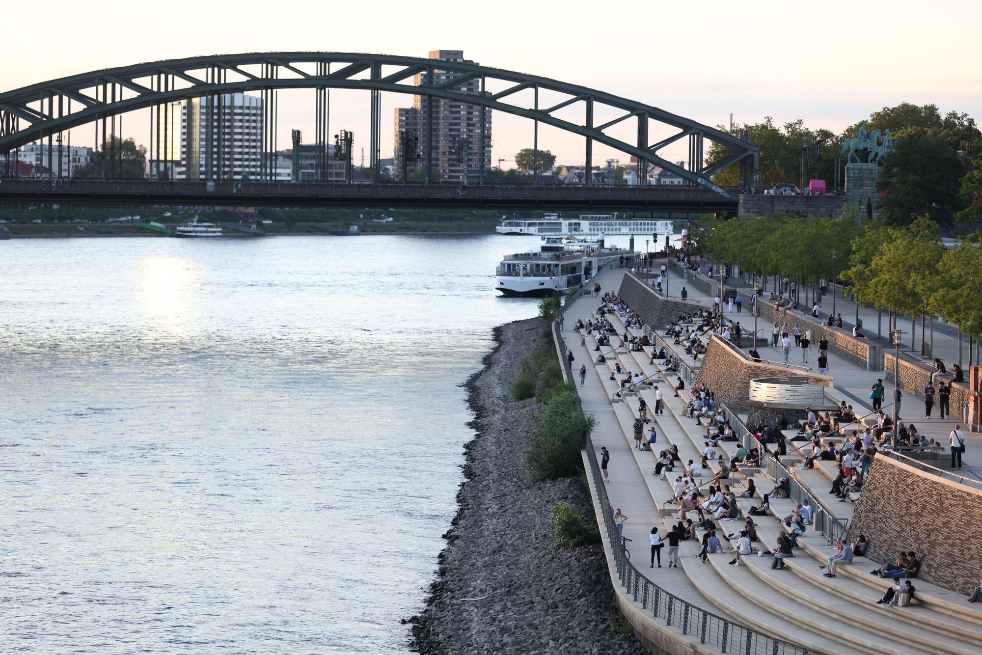 Menschen genießen bei sommerlichen Temperaturen den Blick auf Rhein und Dom am Rheinboulevard. Die Temperaturen des Flusses sind angestiegen.